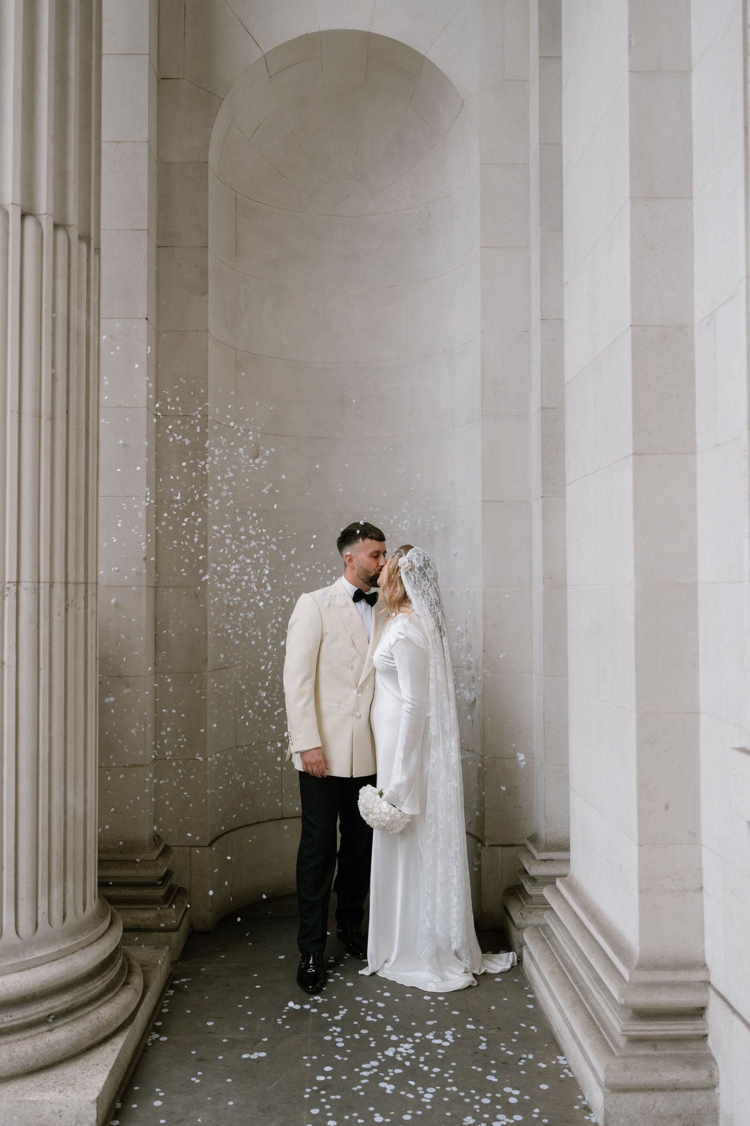 Romantic wedding portrait between classical columns with confetti falling around couple.