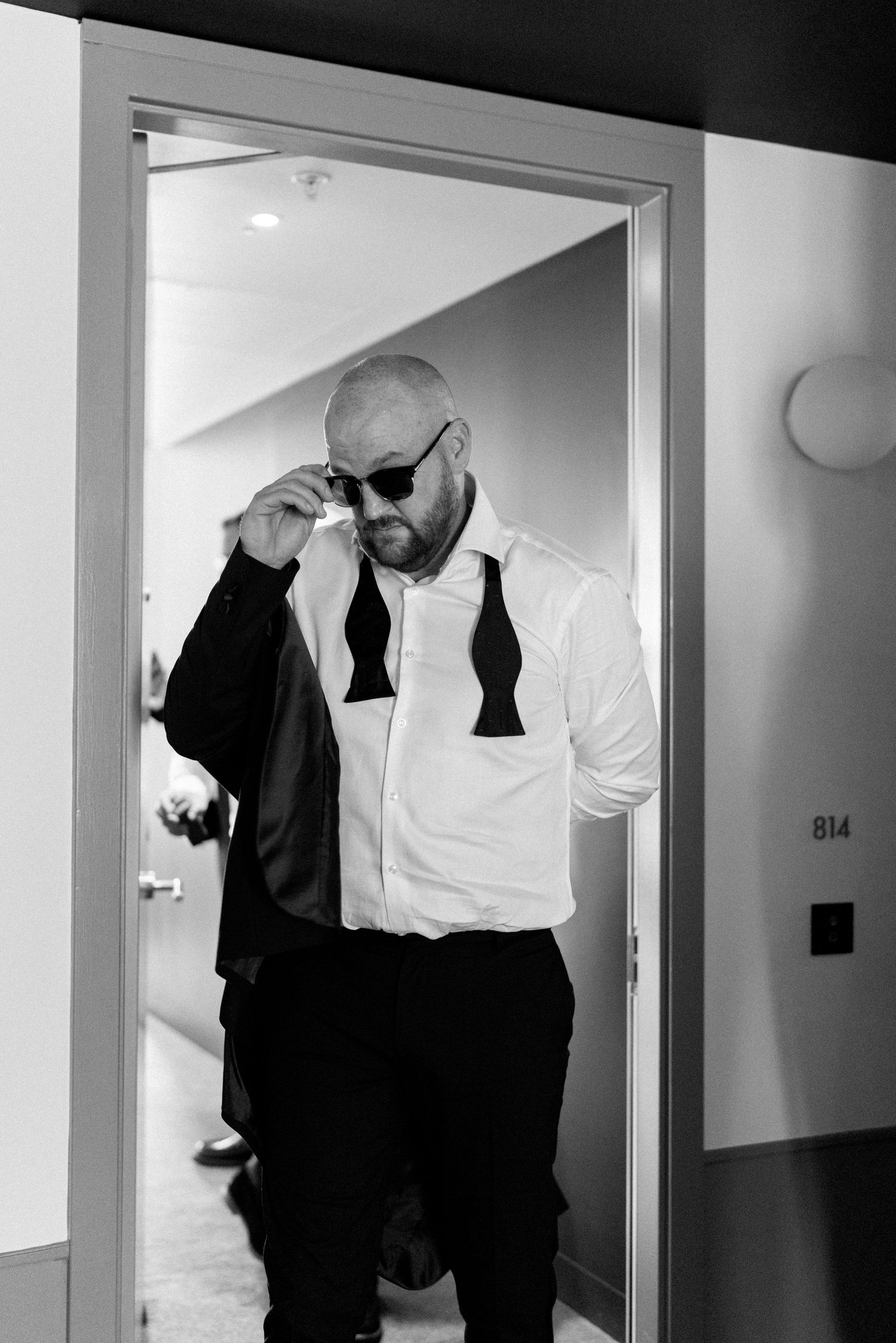 Groomsmen in black suits and white shirts pose playfully in a hotel hallway.