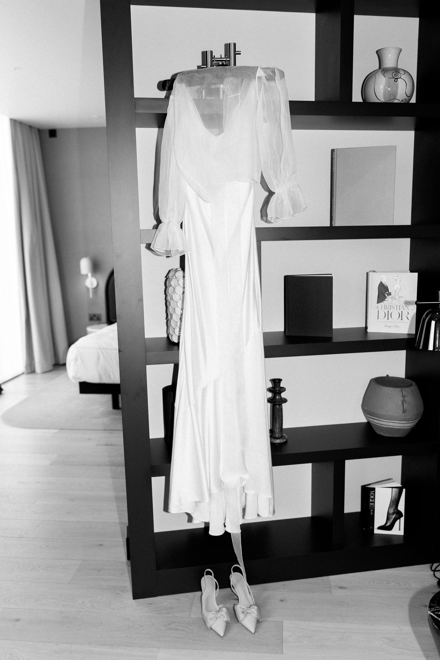 Series of white garments displayed on black wall-mounted shelves in a minimalist interior space.