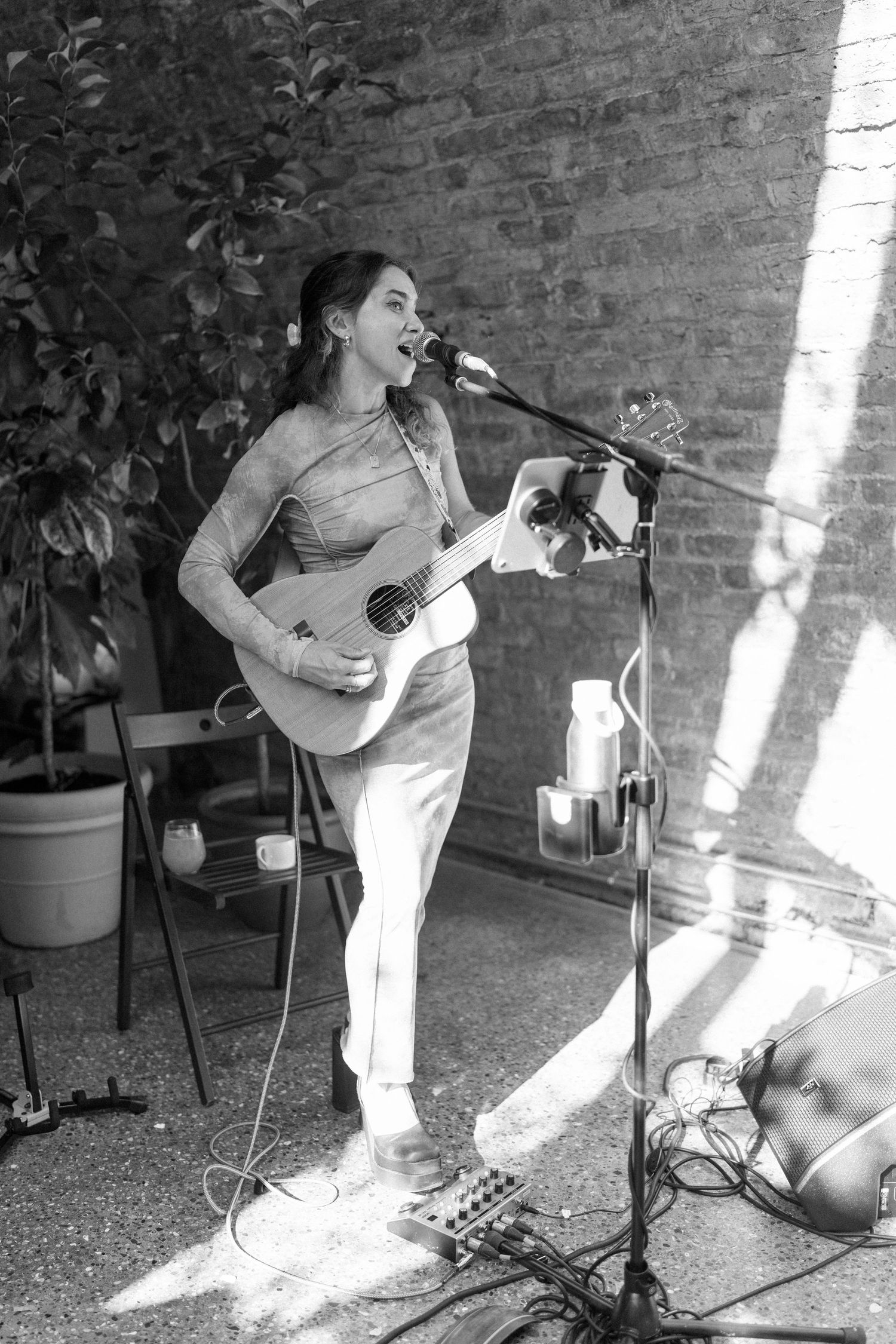 A musician performs with a guitar against a brick wall in black and white.