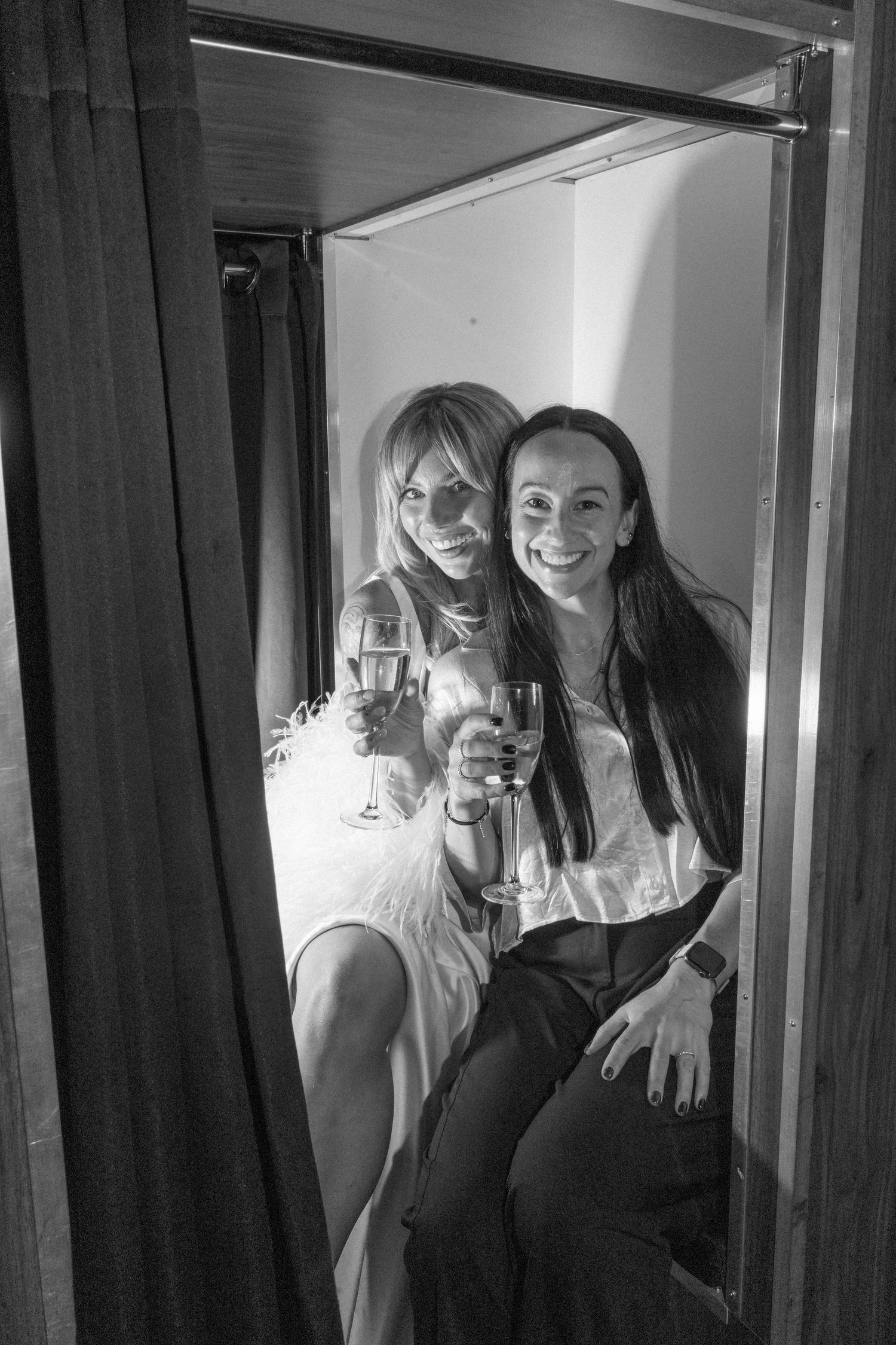 Two wedding guests share drinks and smiles in a black and white photo booth style shot.