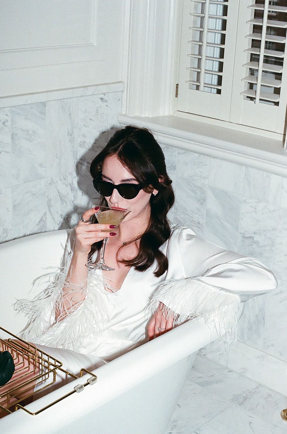 A person wearing sunglasses relaxes in a luxurious white marble bathtub.