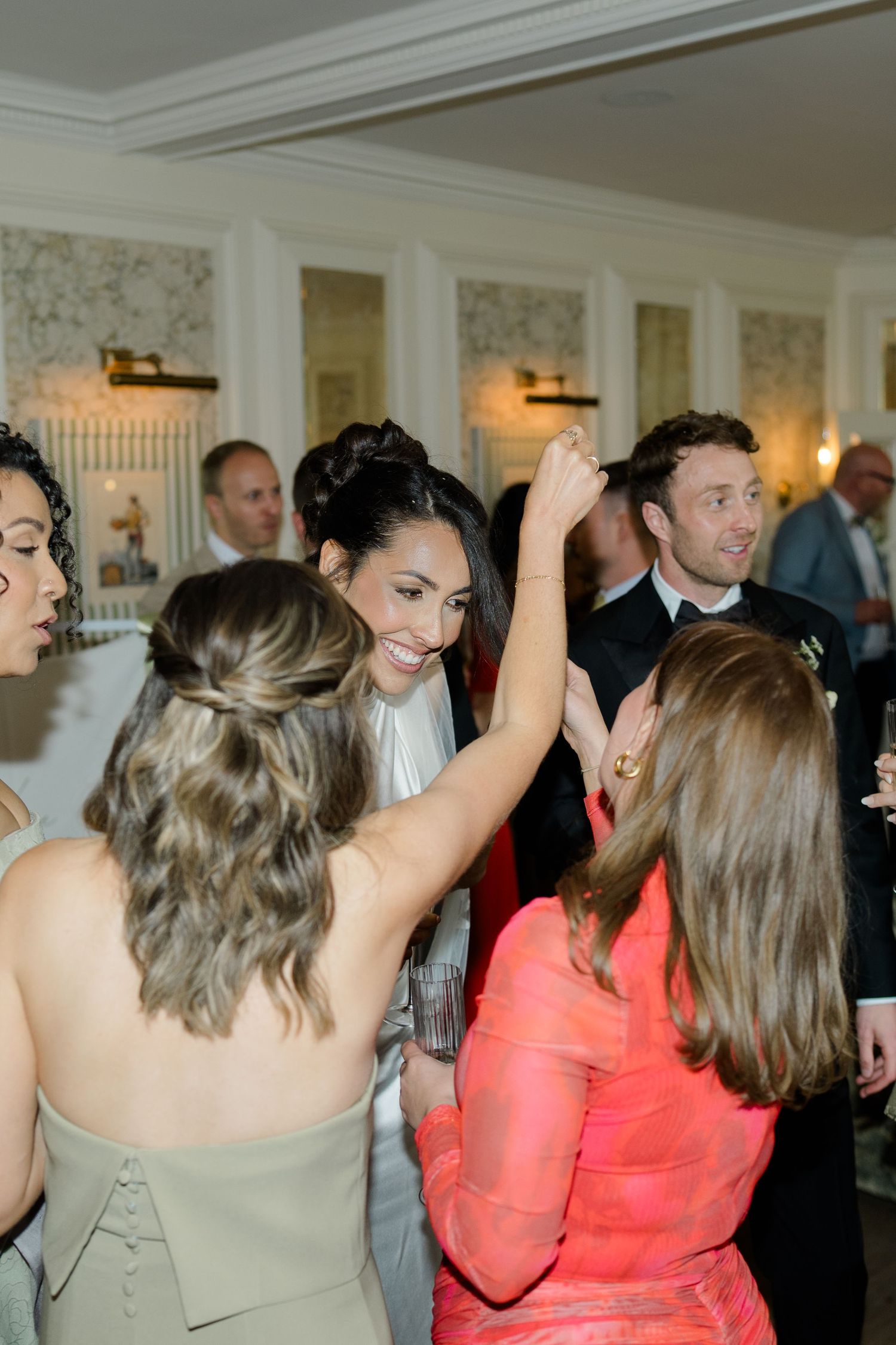 Bride laughing and dancing with guests during lively wedding reception in elegant white decorated venue.