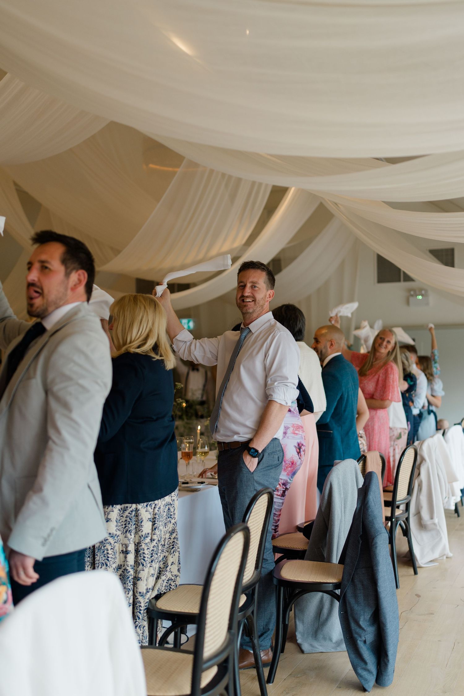 Elegantly dressed wedding guests mingle and celebrate inside a beautifully draped white marquee reception venue.