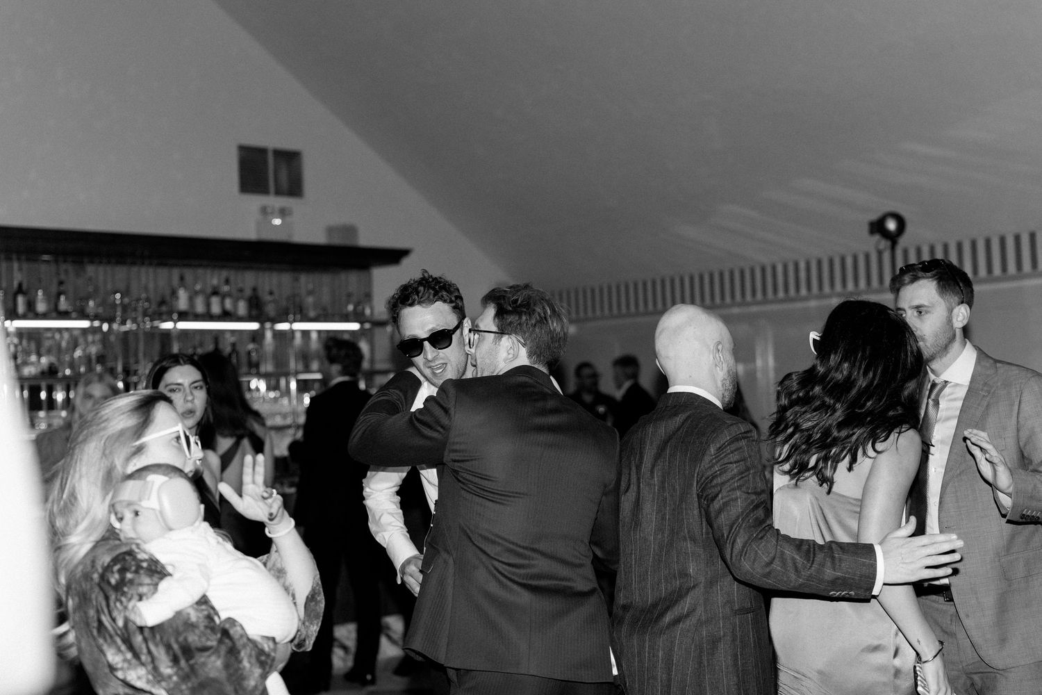 Black and white photo of wedding guests dancing and embracing joyfully at a lively reception.