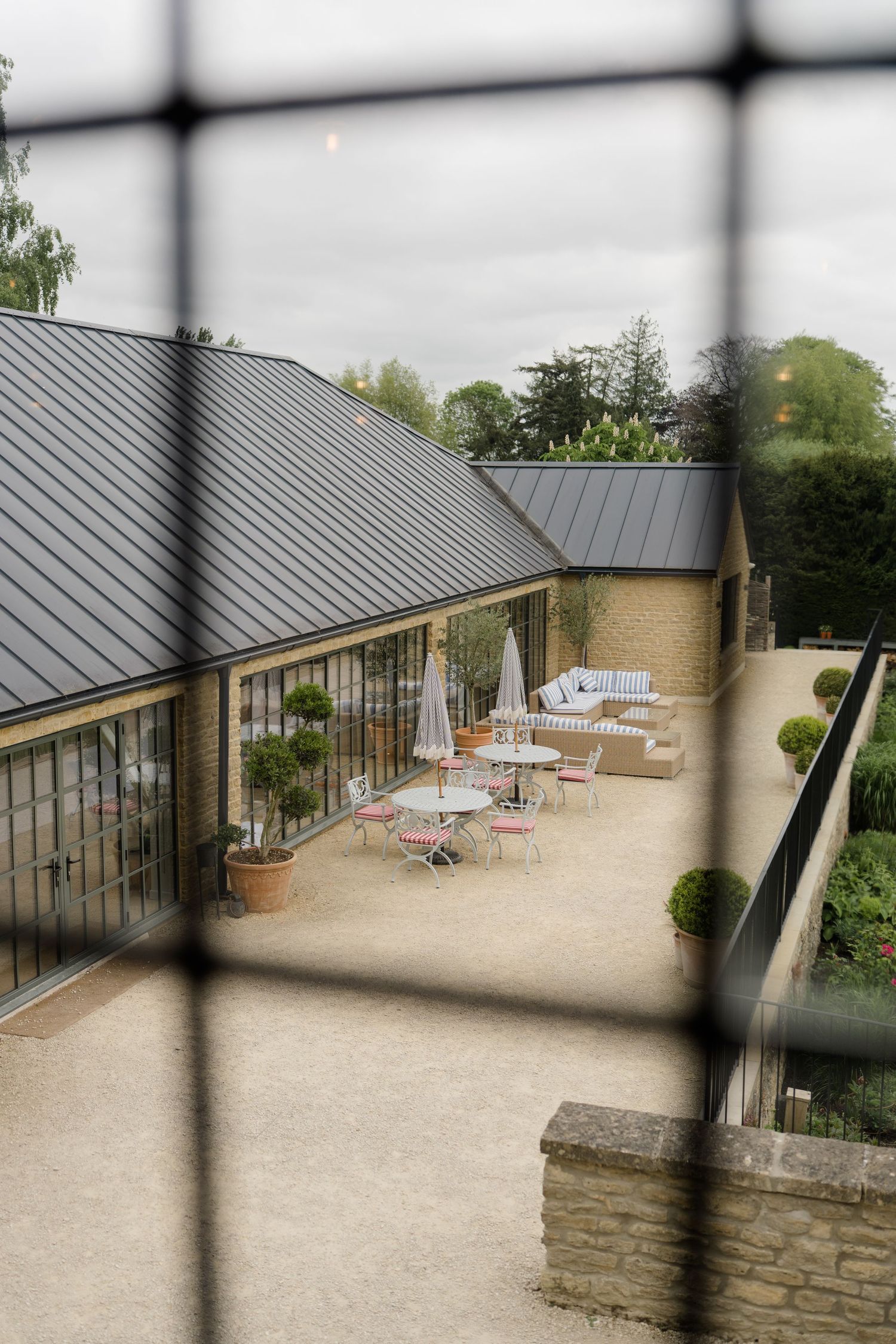 Elegant outdoor terrace of a stone venue with bistro tables, patio umbrellas, and manicured topiary hedges.