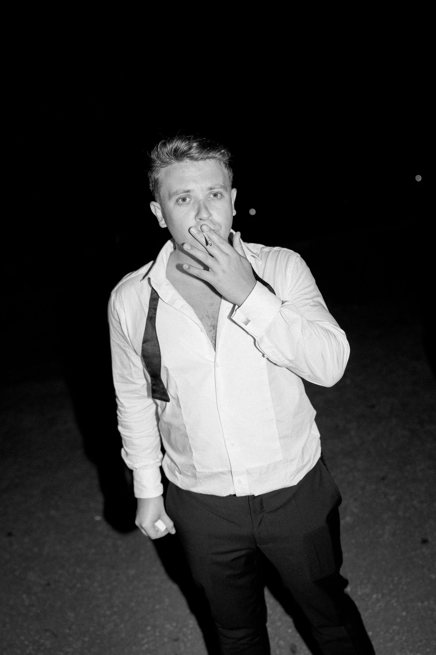 Black and white nighttime portrait of a man in a white shirt and loosened tie outdoors.