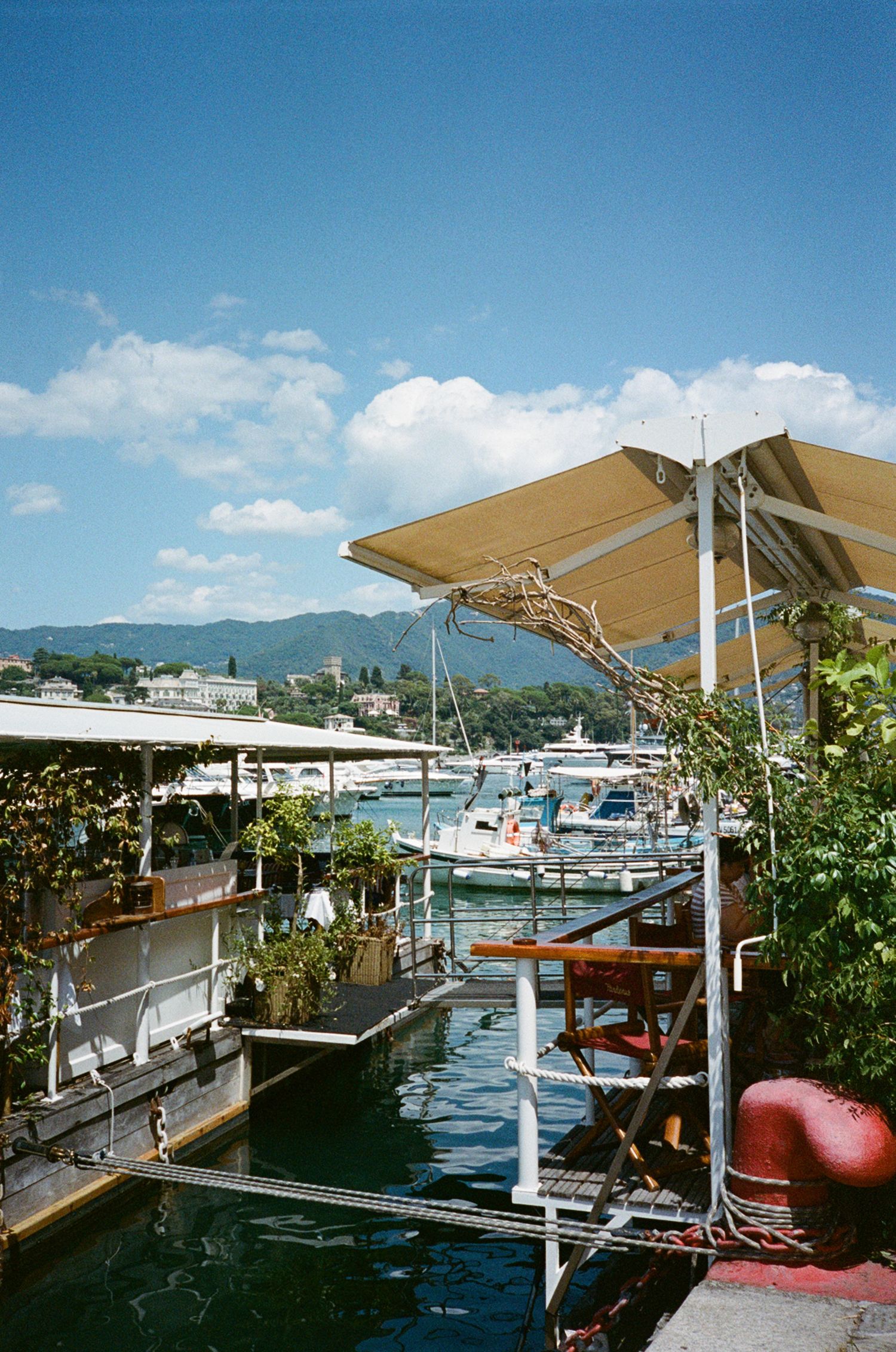 Scenic Italian marina with boats, floating dock, and lush hillside backdrop on a sunny day.
