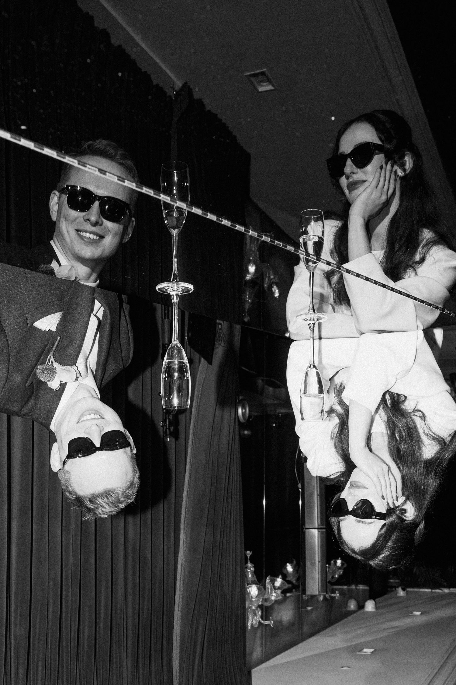 Black and white photo of bride and groom laughing at a bar with microphones.