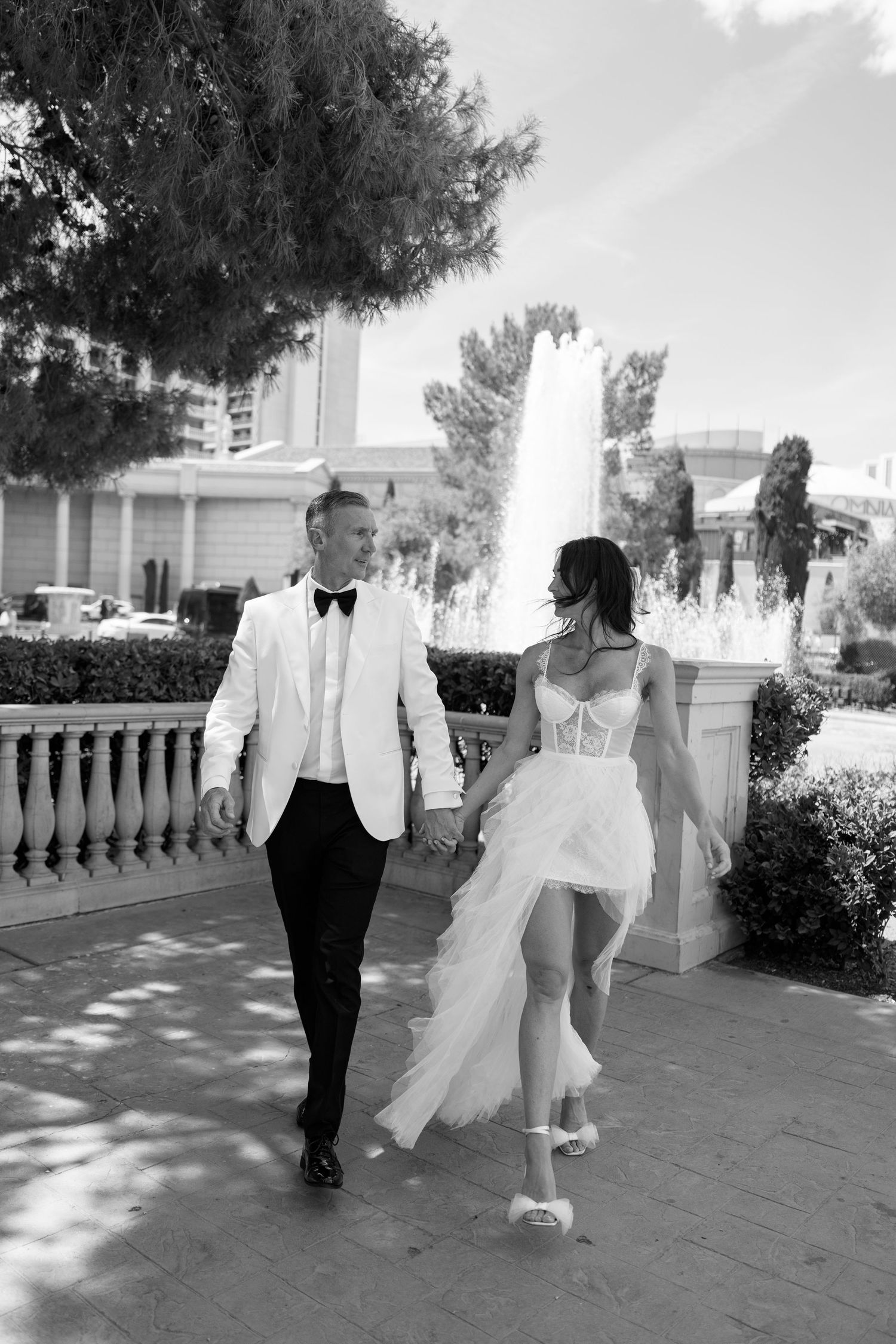 Black and white photo of couple walking through garden colonnade in wedding attire.