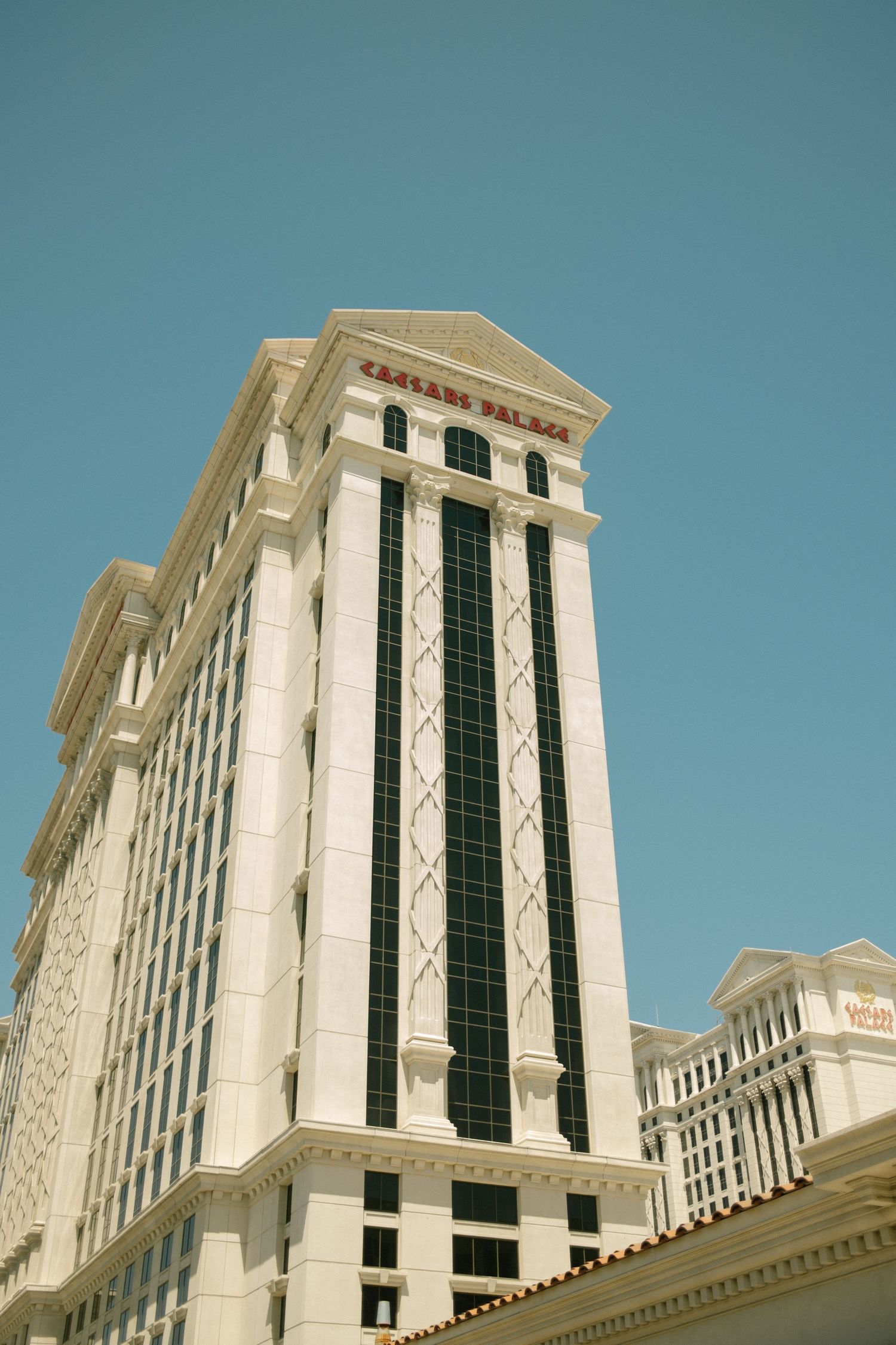 Exterior view of Caesars Palace hotel tower with classic Roman architecture against blue sky.