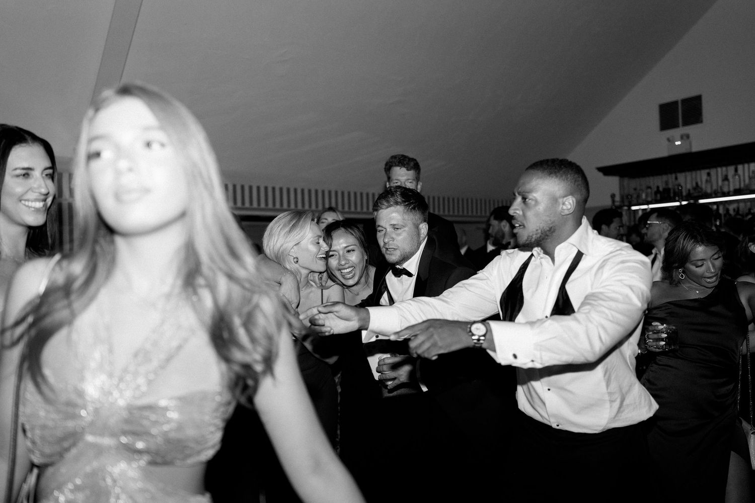 Wedding guests dance and celebrate joyfully on the dance floor in a black and white photo.