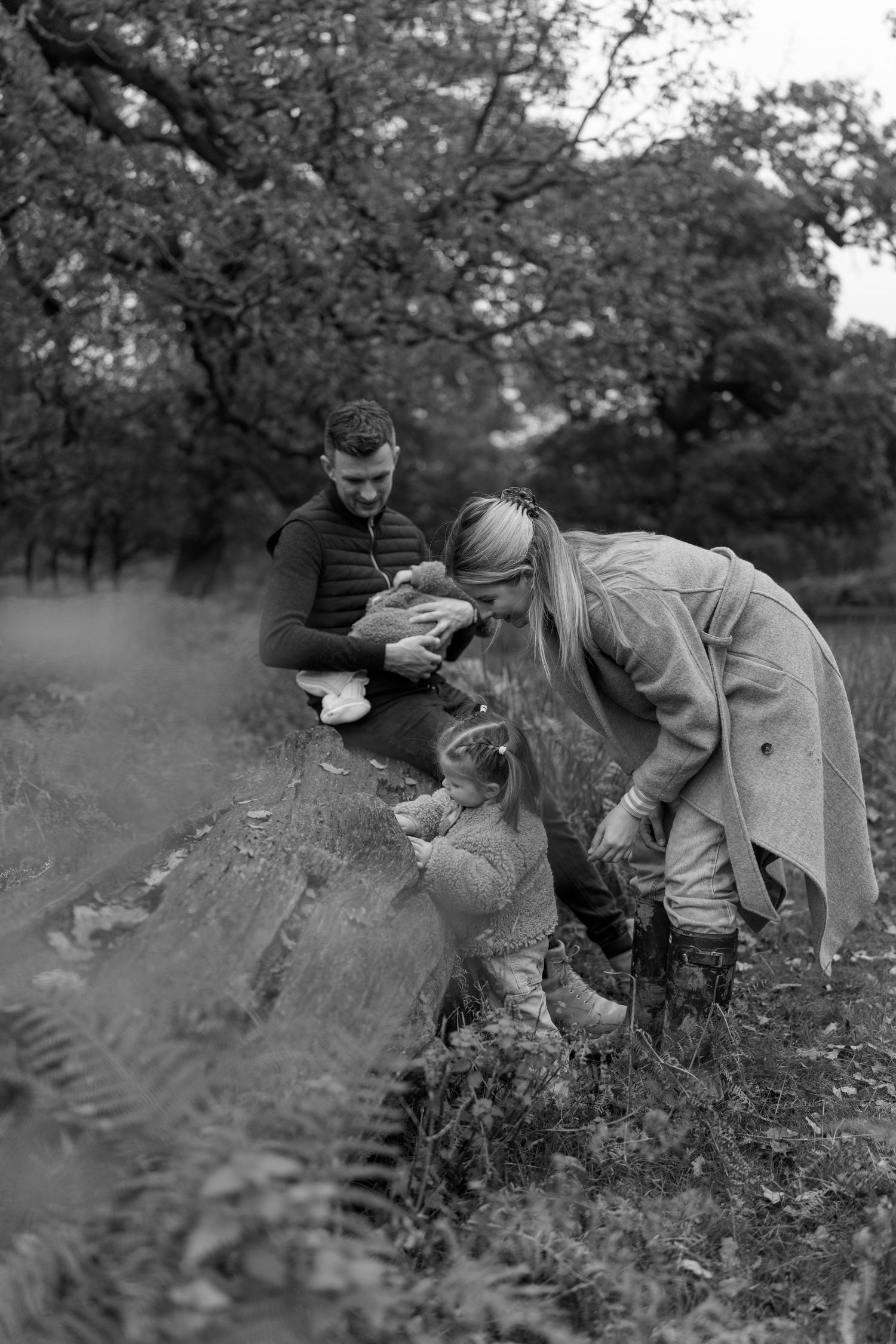 Family members interact in a natural outdoor setting among ferns and foliage.
