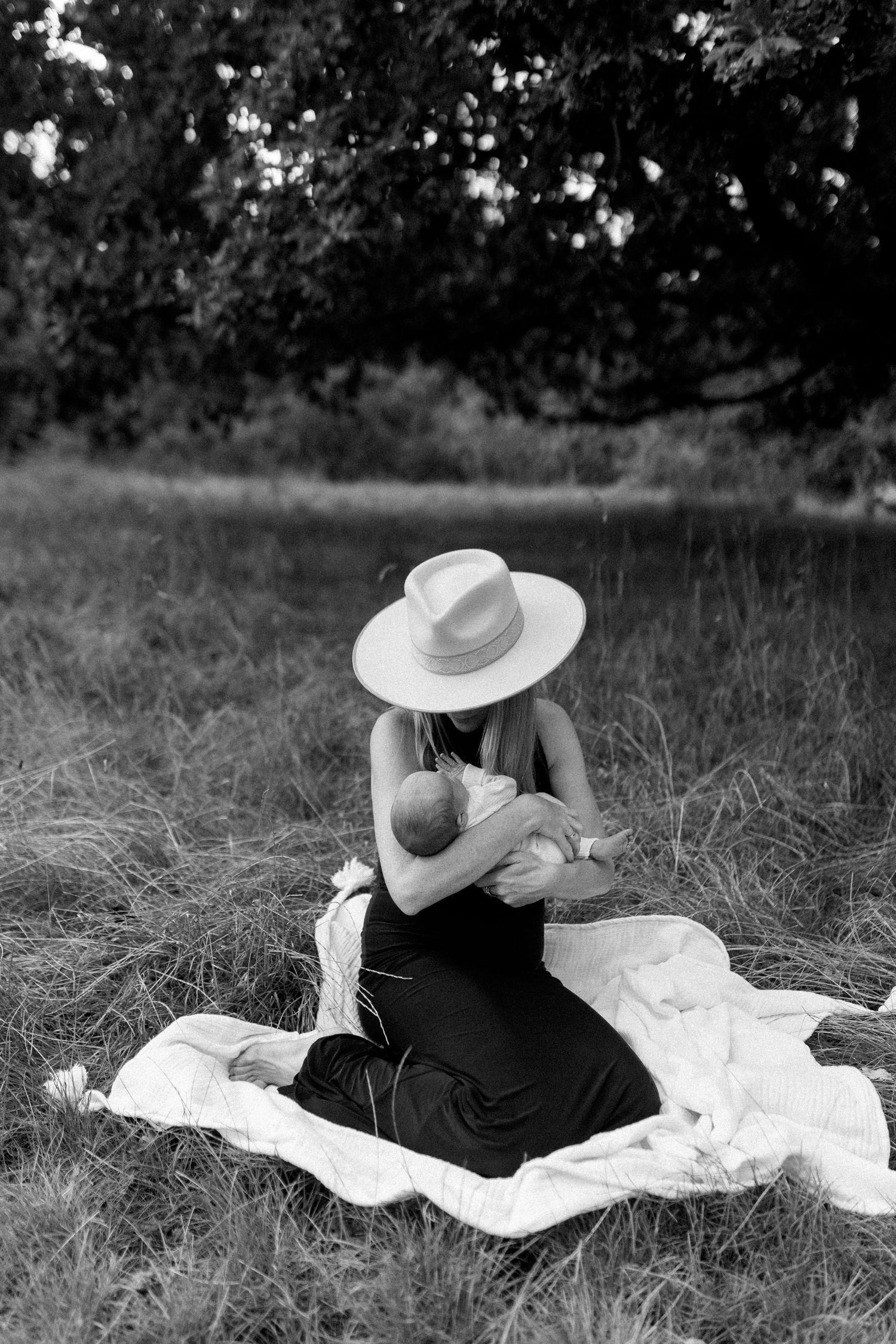 Person in black dress and white hat lounging on blanket in grassy field.