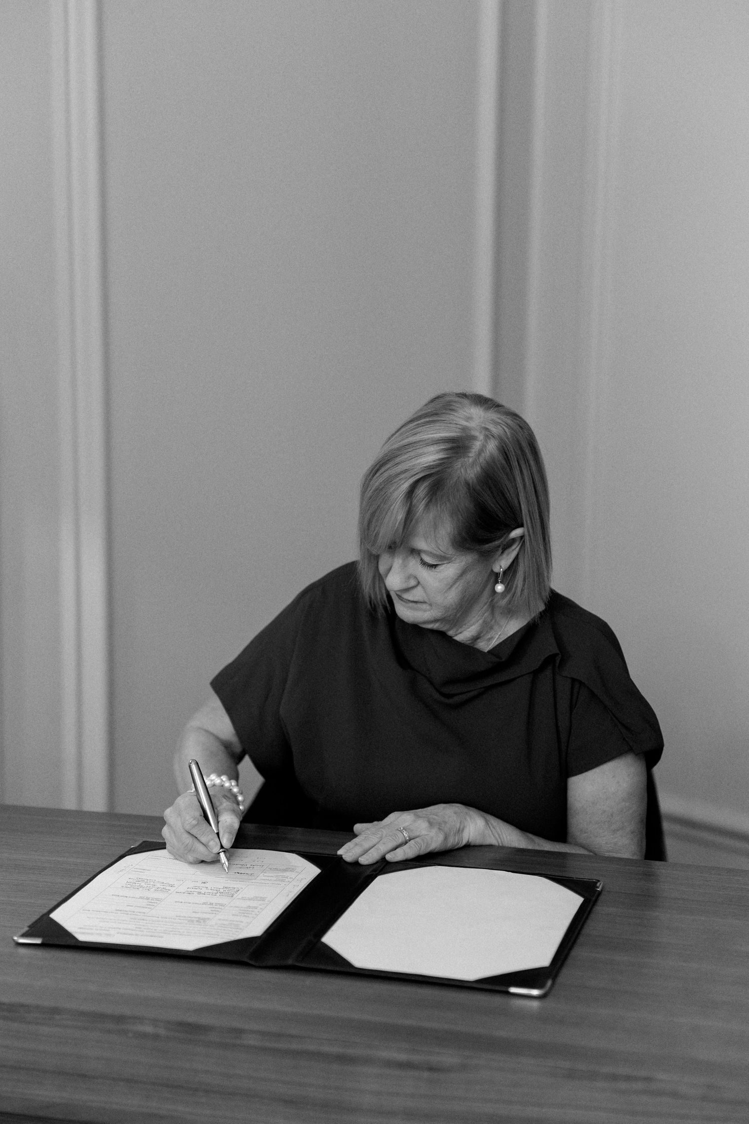 Series of black and white photos showing someone signing documents at a wooden table.