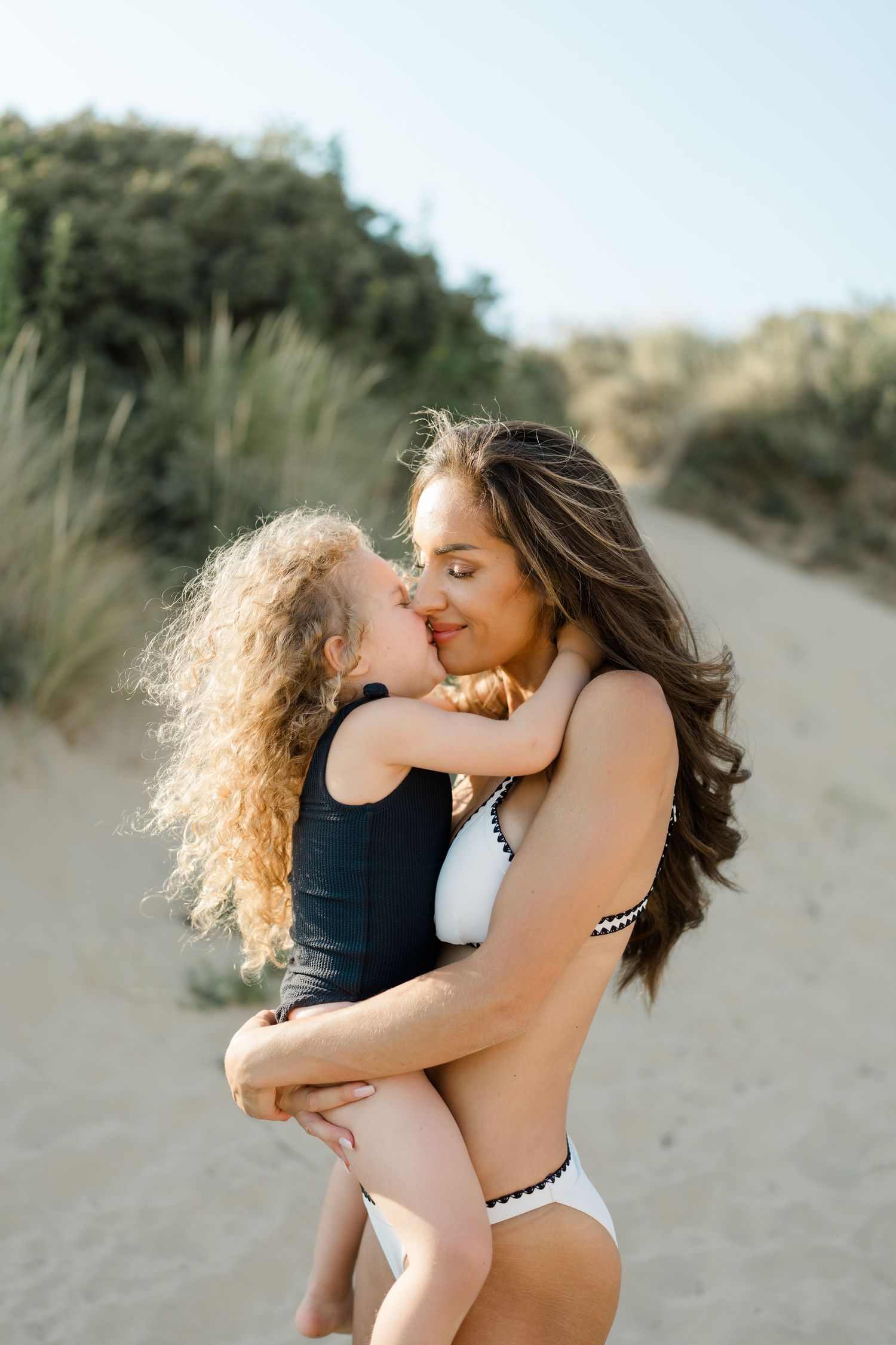 Tender moment captured between parent and child embracing on sandy beach dunes.