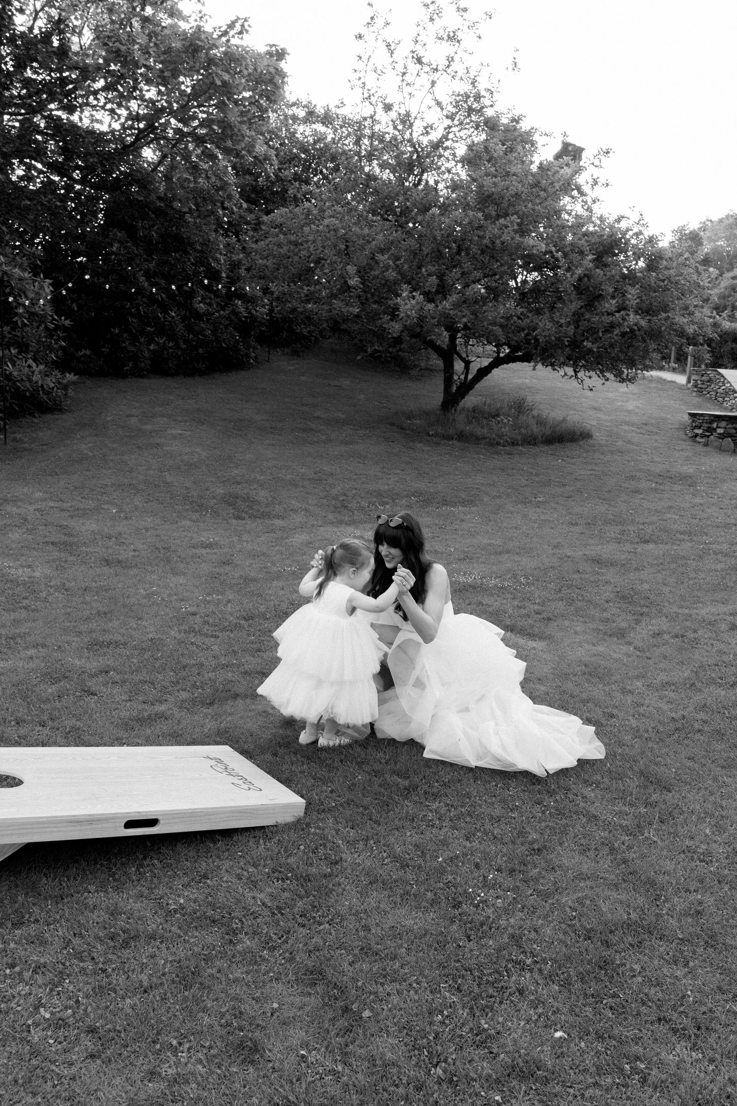 Two people in wedding attire lay on a white surface outdoors on grass.