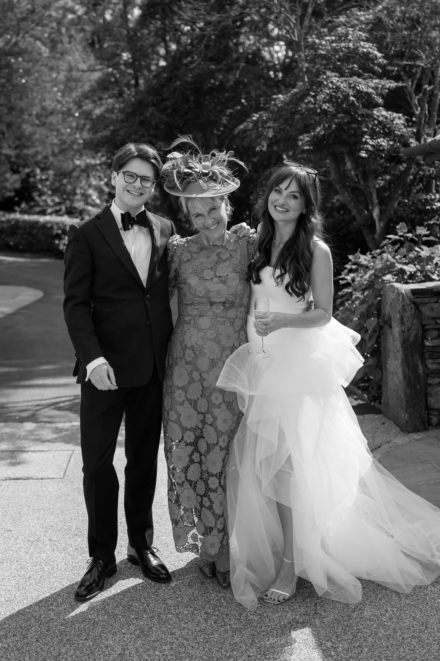 Black and white wedding photos taken in front of a stone pillar in a garden setting.