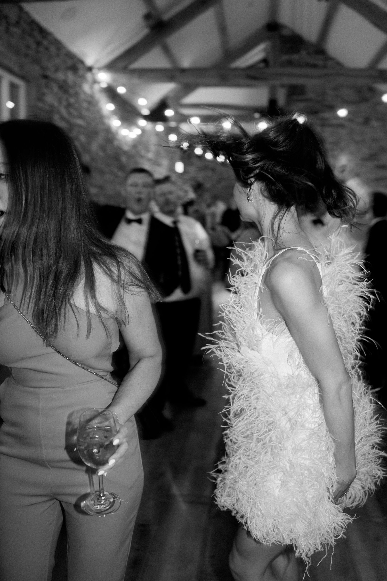 Partygoers in elegant attire dancing and holding drinks at a festive indoor celebration.
