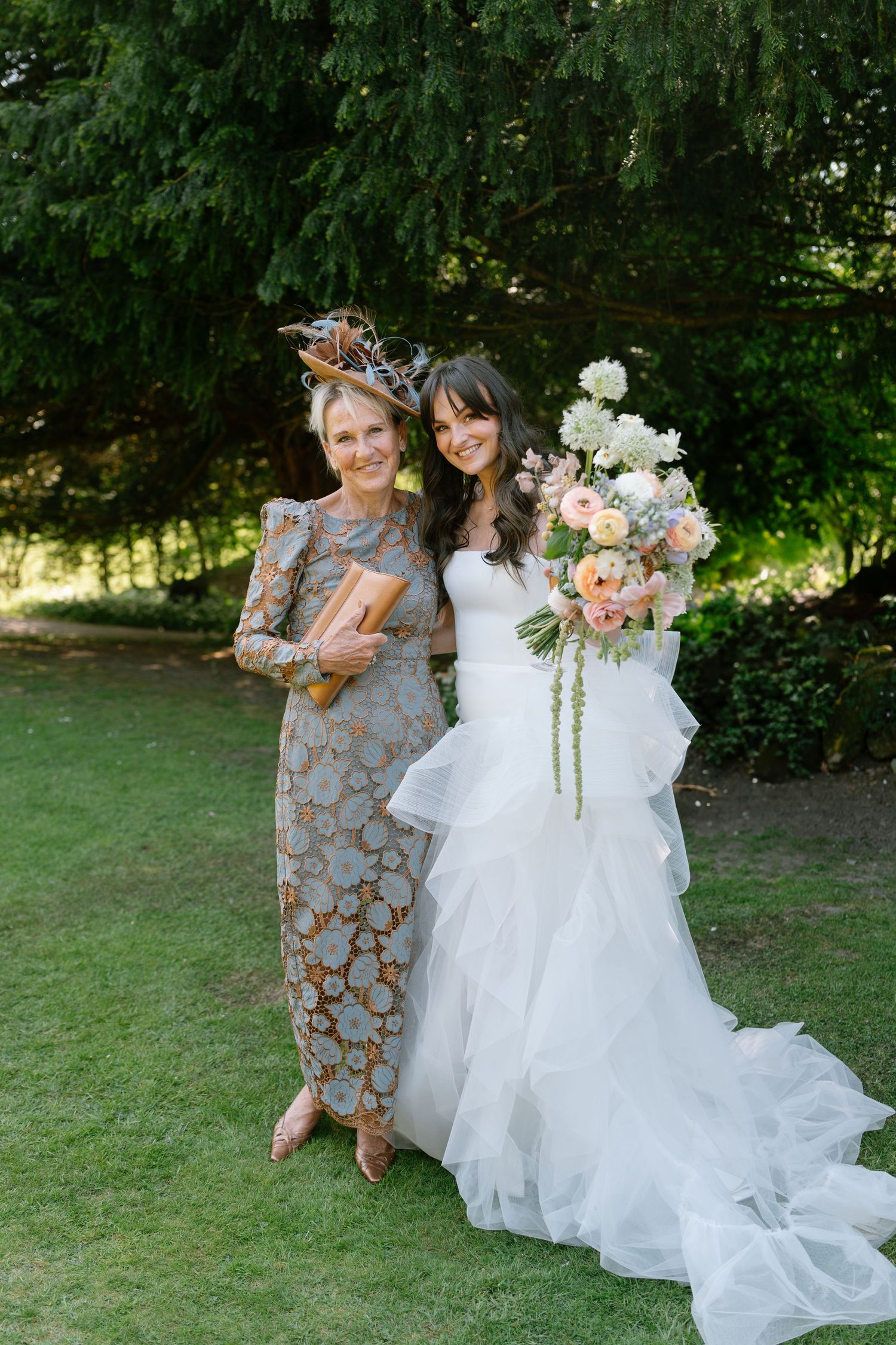 A flowing white wedding dress trails across green grass during outdoor photography session.
