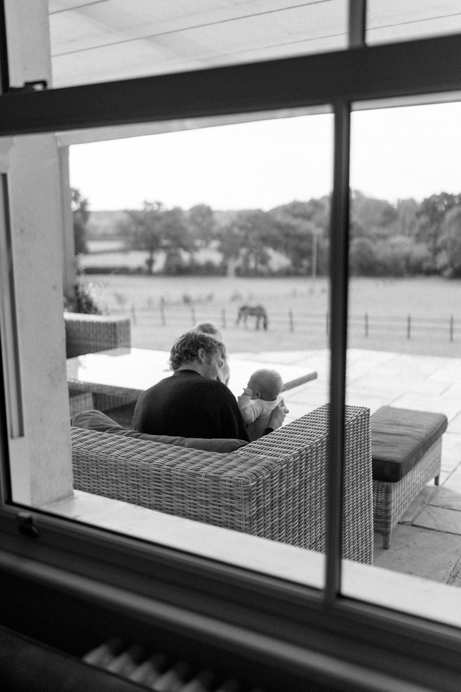 Black and white view through window showing outdoor seating with pastoral landscape.