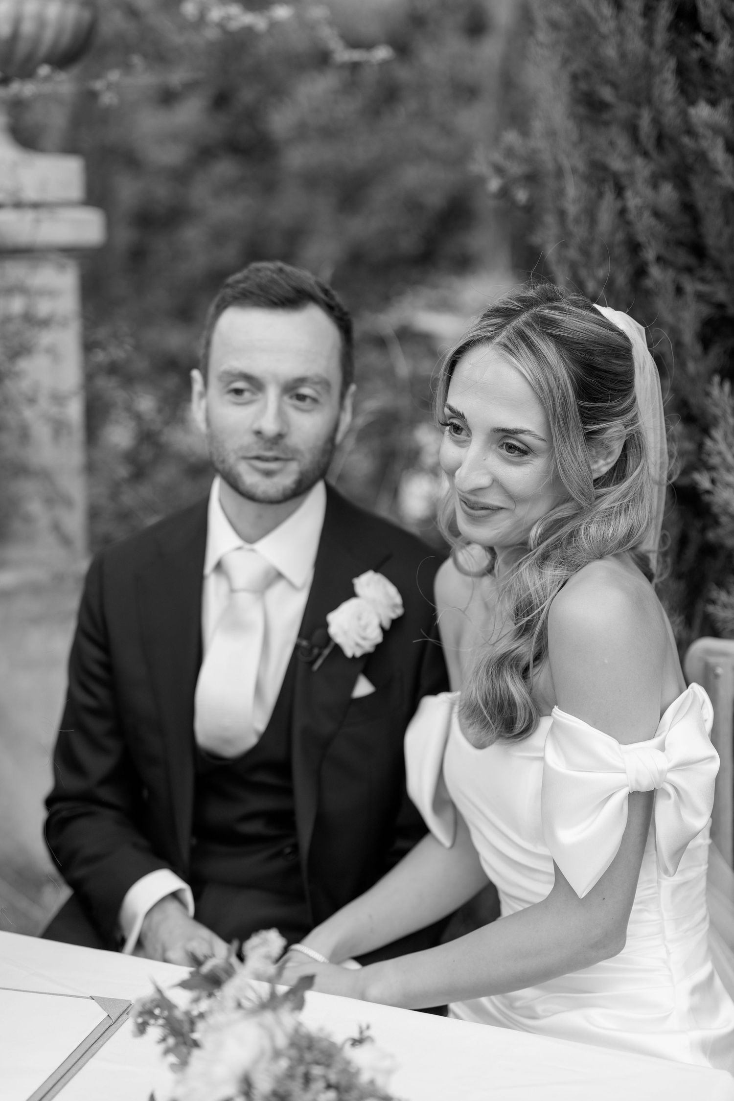 Couple in formal wedding attire sitting at a signing table during their outdoor ceremony.