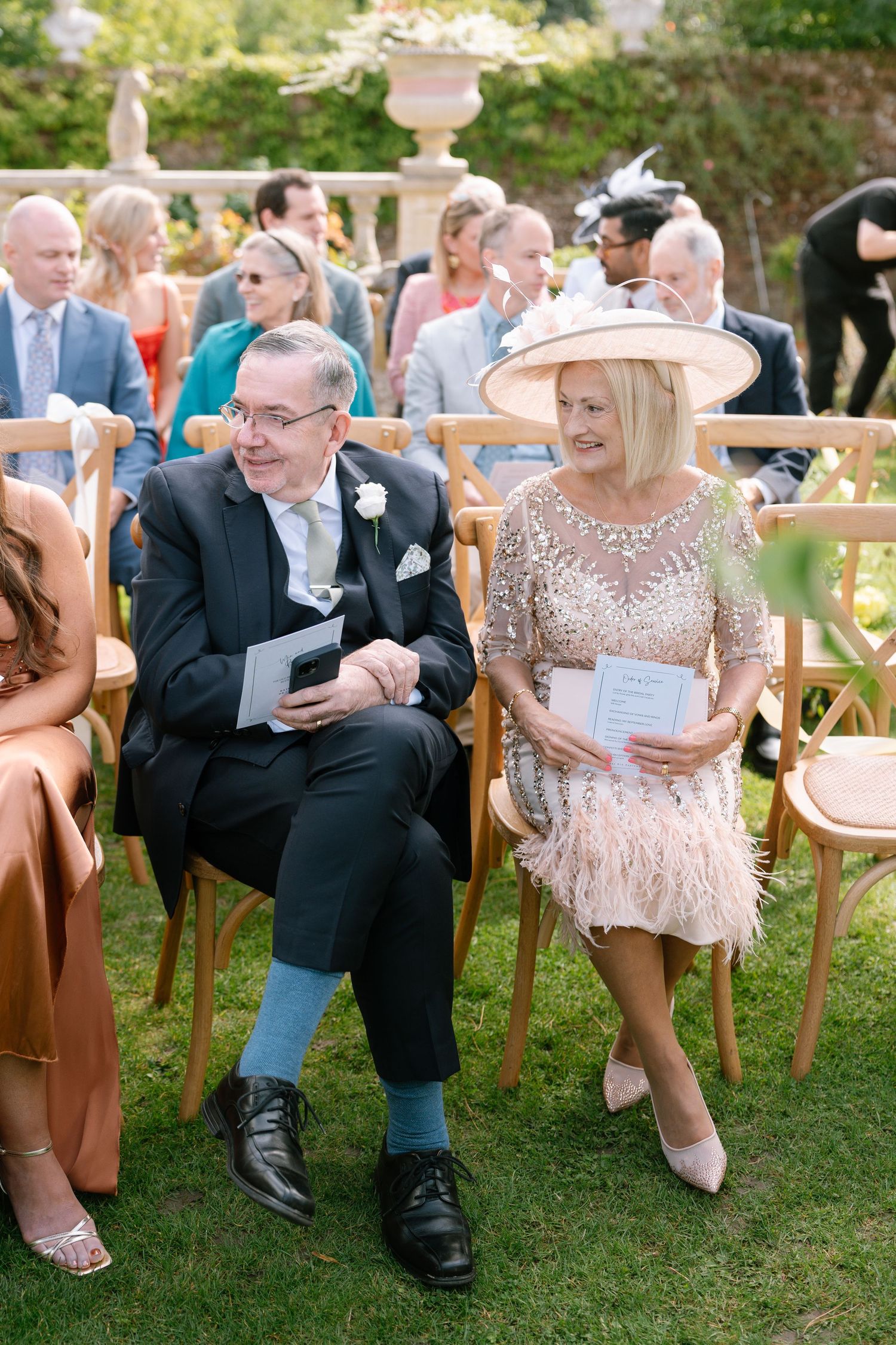 Wedding guests seated in wooden chairs enjoying a casual moment during an outdoor ceremony.