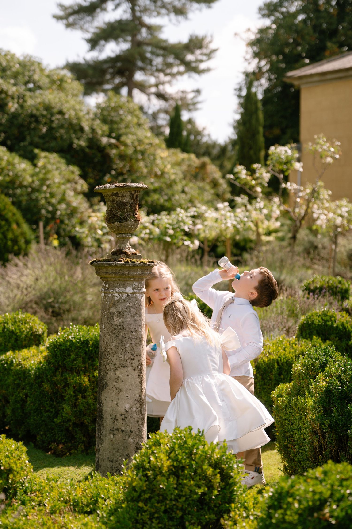 Wedding celebration in a manicured garden with stone pillars and blooming flowers.