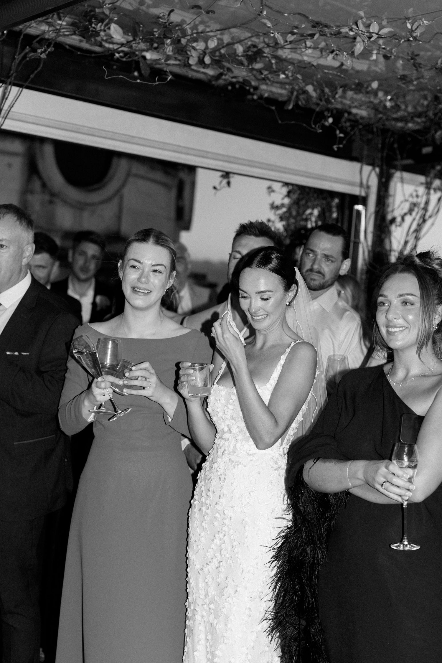 Wedding party members share joyful moments during an indoor celebration with decorative lighting.