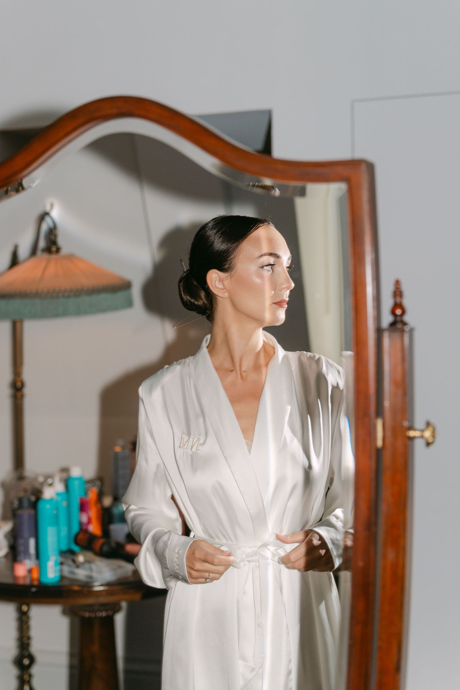 Person in white silk robe posing in front of mirrors in bathroom.