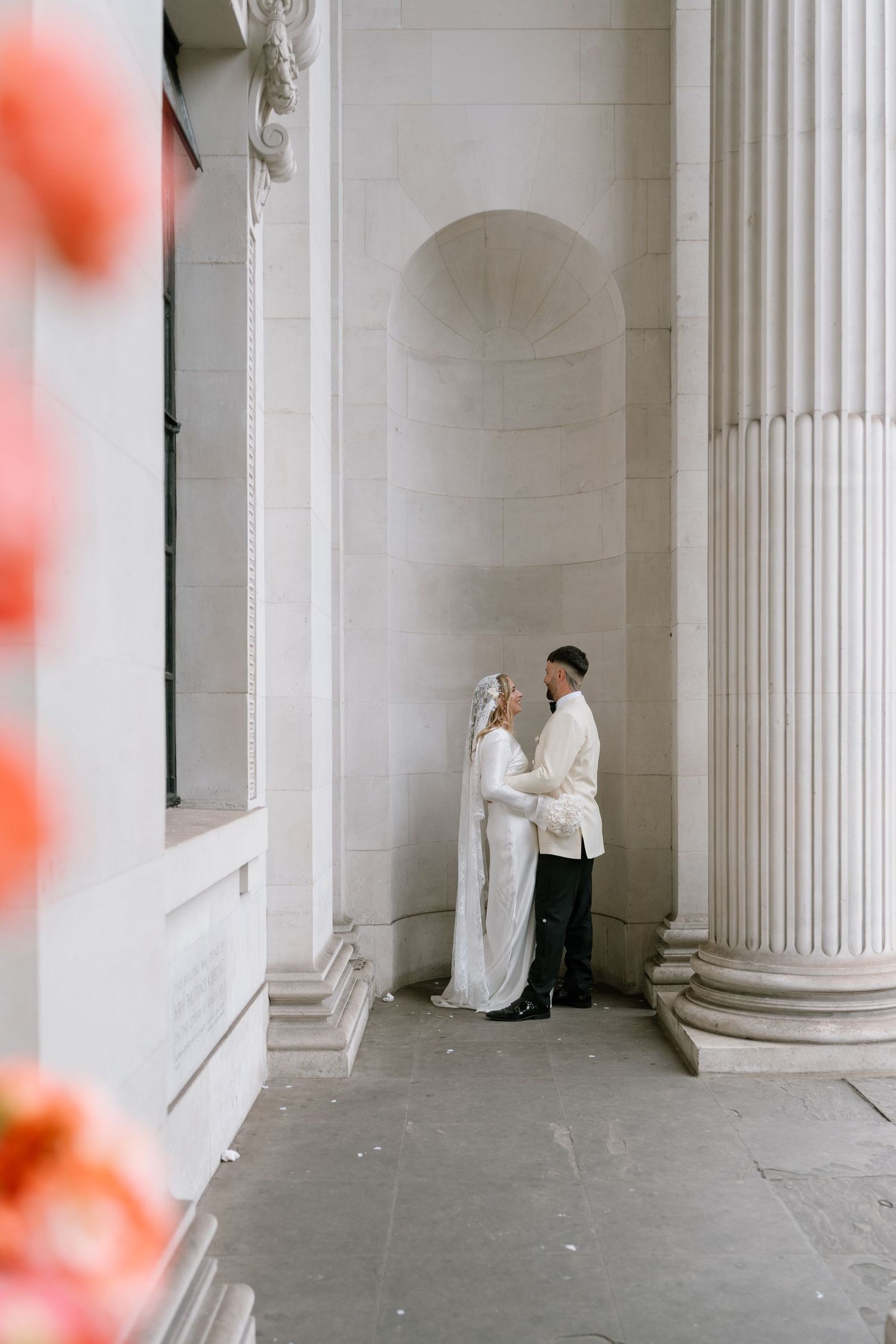 Couple shares an intimate moment between classic white columns in a soft-focus shot.