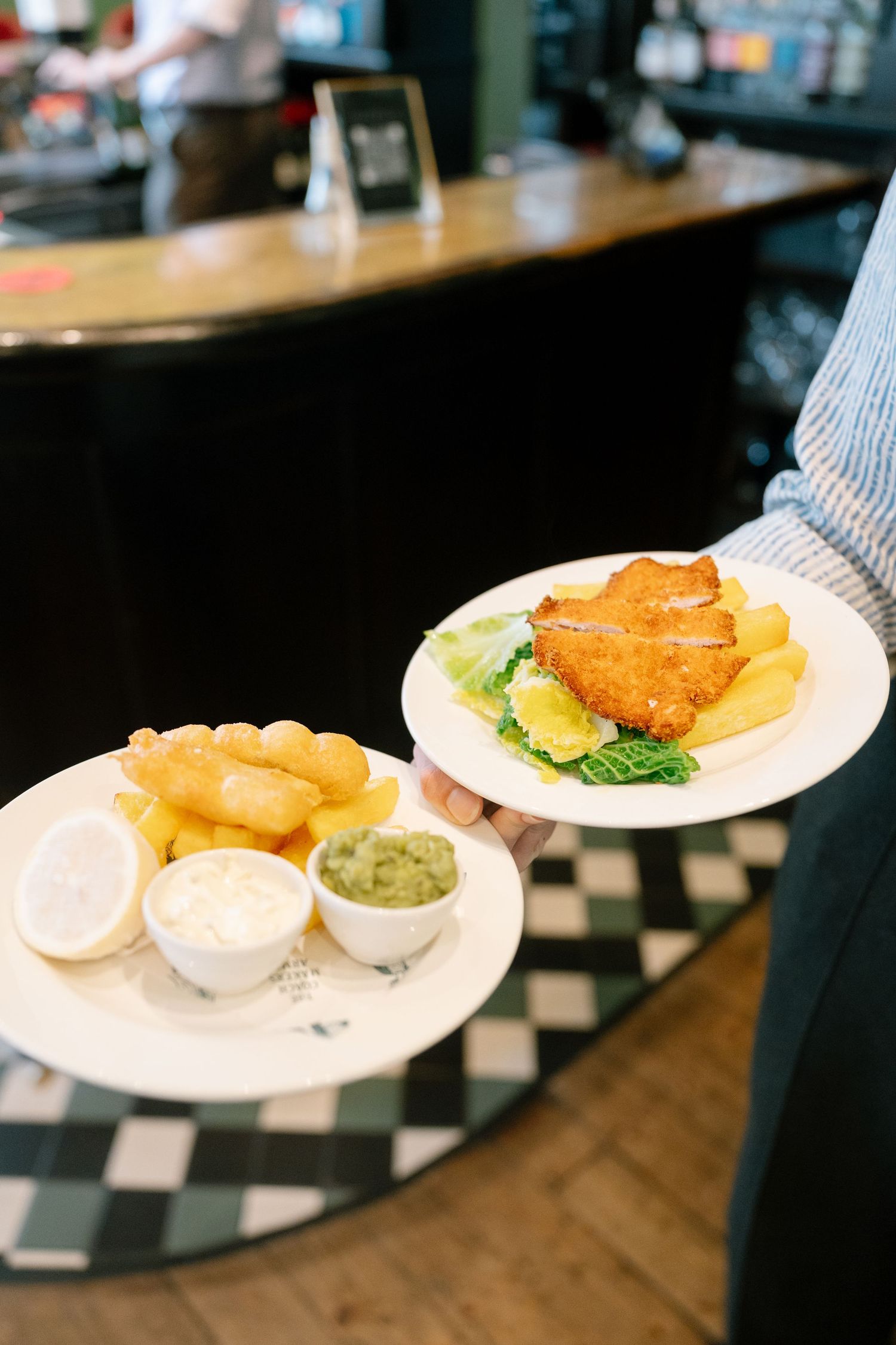 Sequence of plated dishes including fish and chips with tartar sauce on a checkered counter.