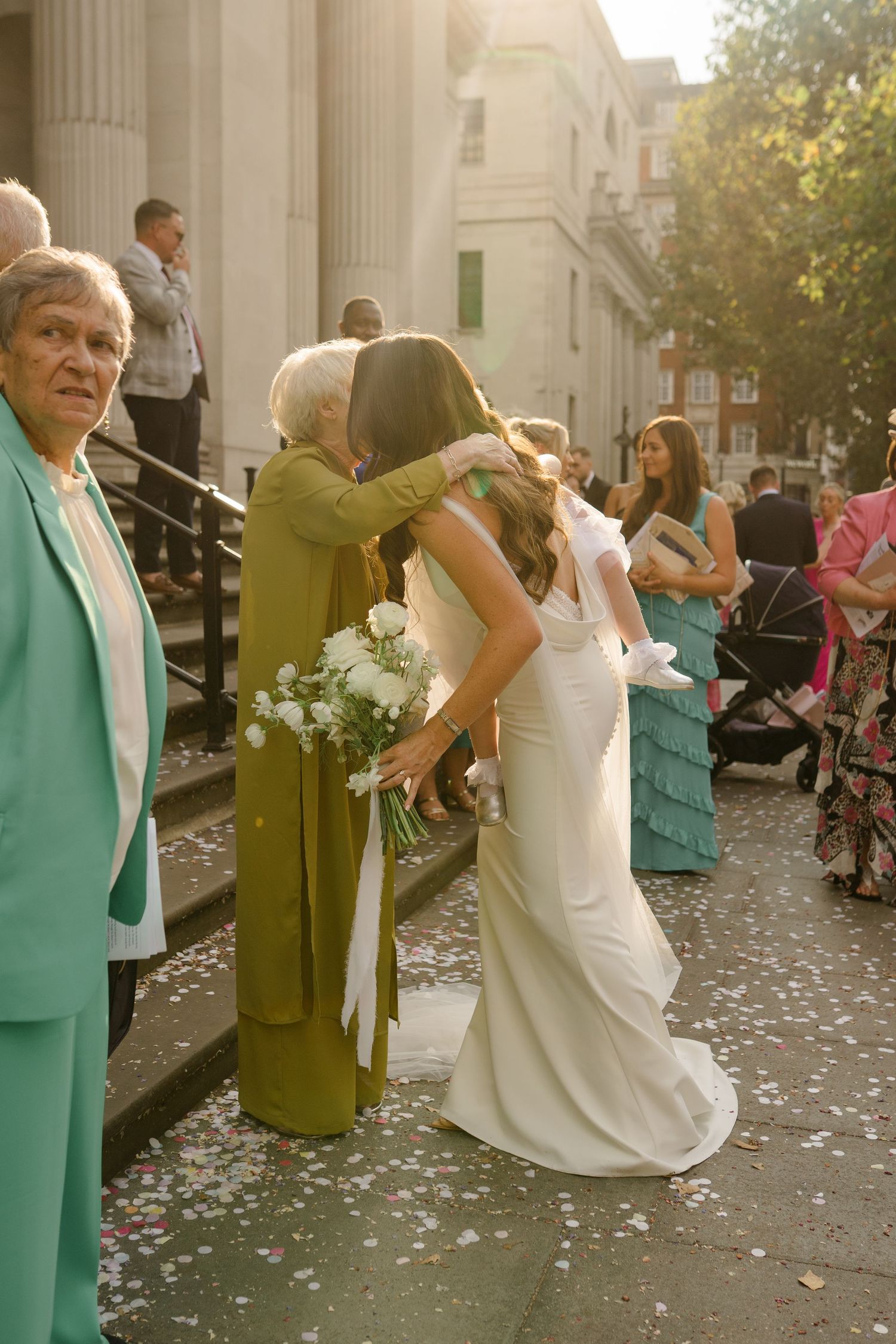 Wedding guests in mint green and white attire gather on elegant stone steps.