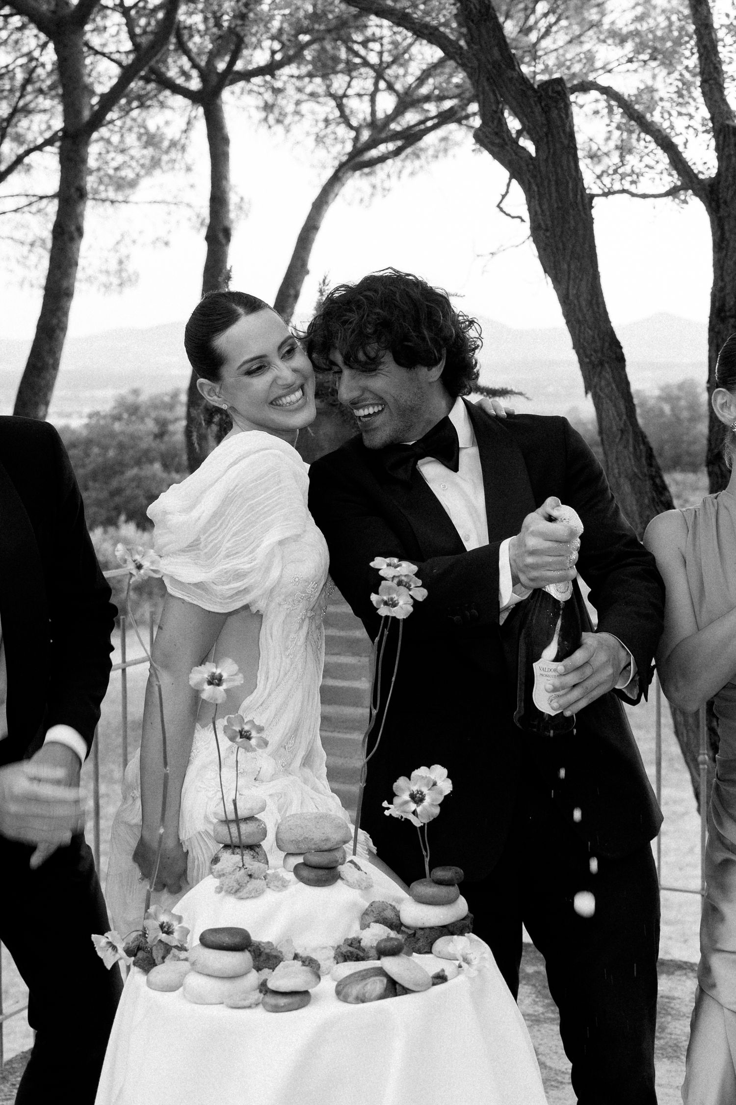 Wedding party enjoying candid moments during an outdoor celebration under trees.