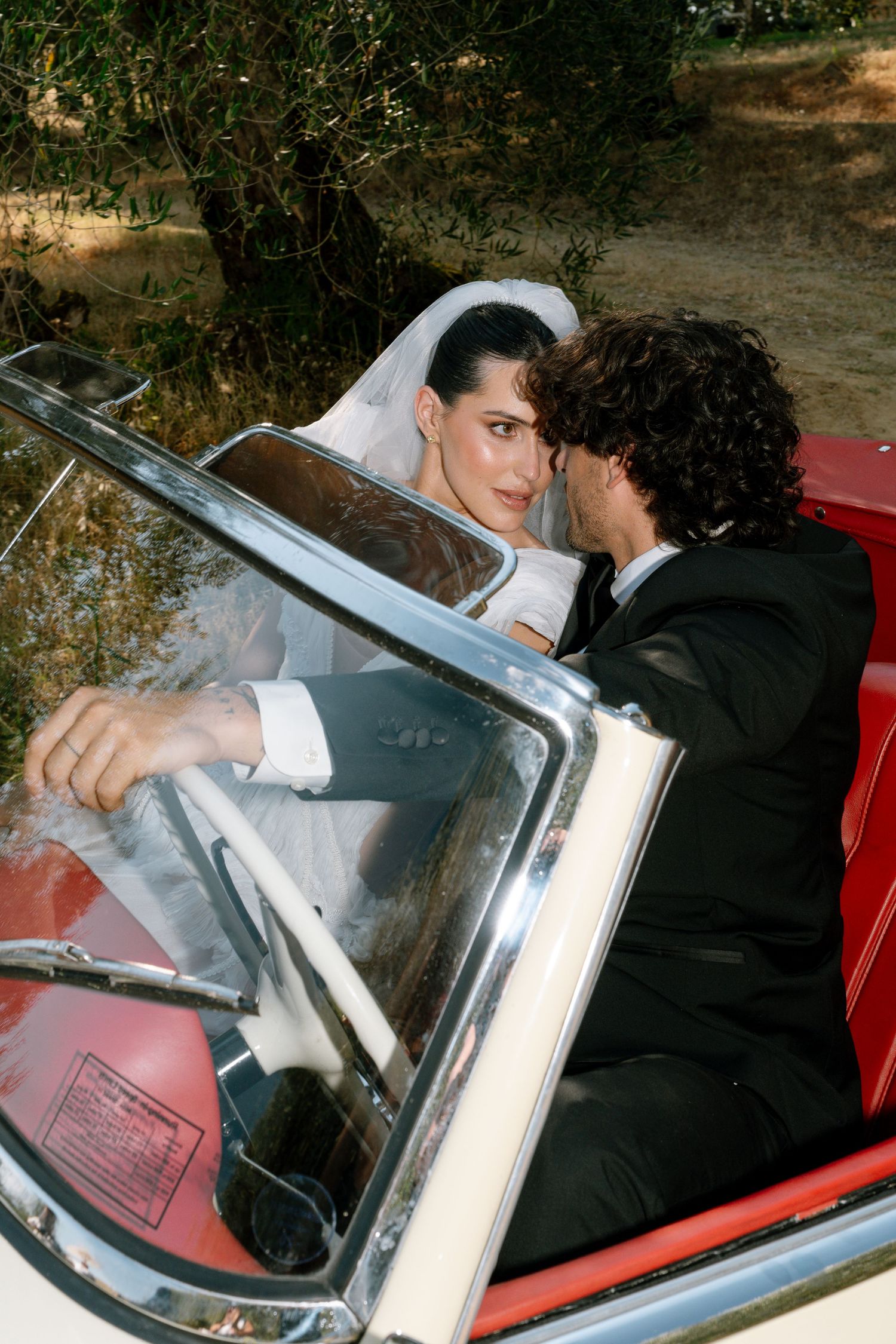A couple seated in a classic convertible car with red interior.