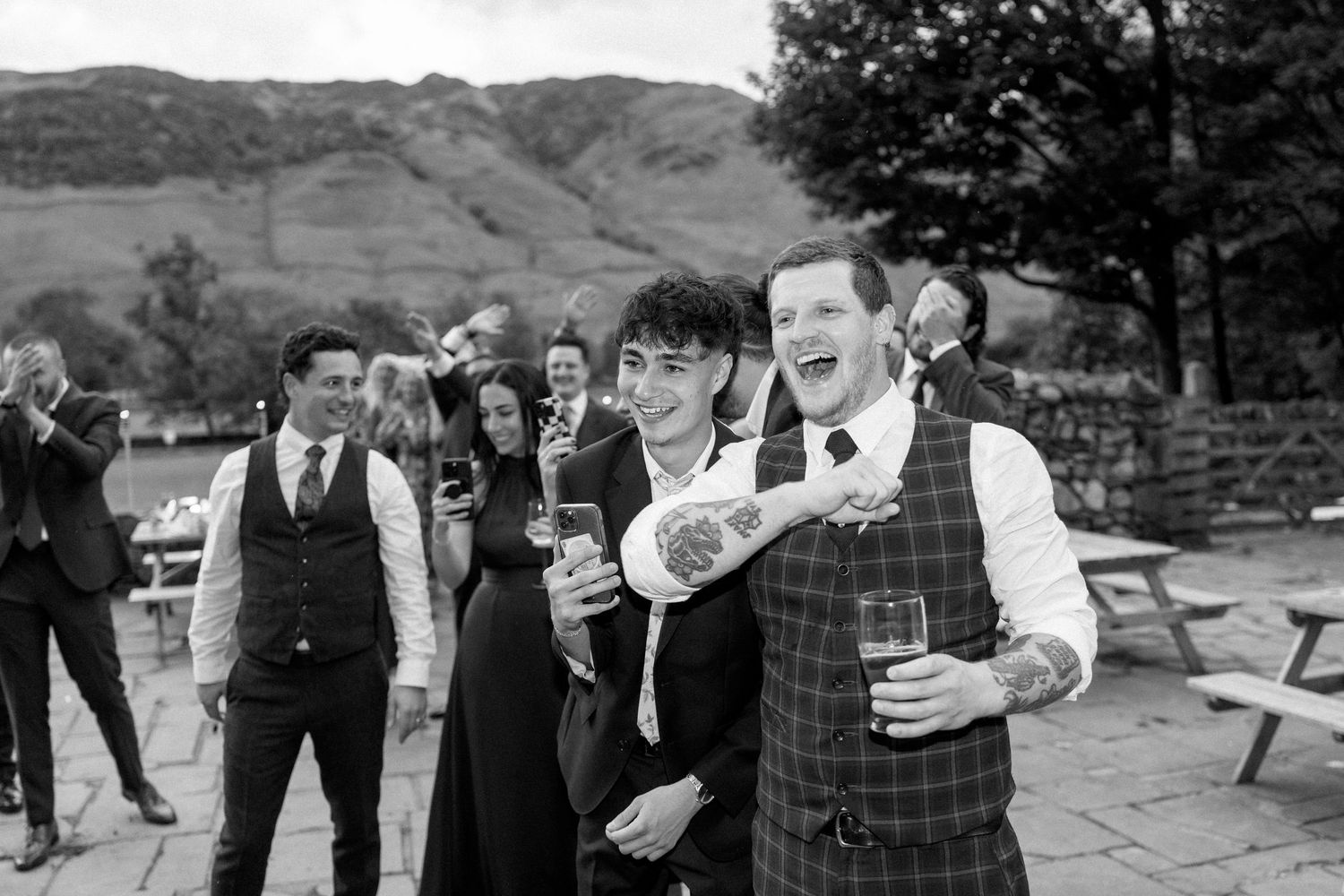 Wedding guests in formal attire enjoying drinks and conversation on an outdoor patio with mountain views.