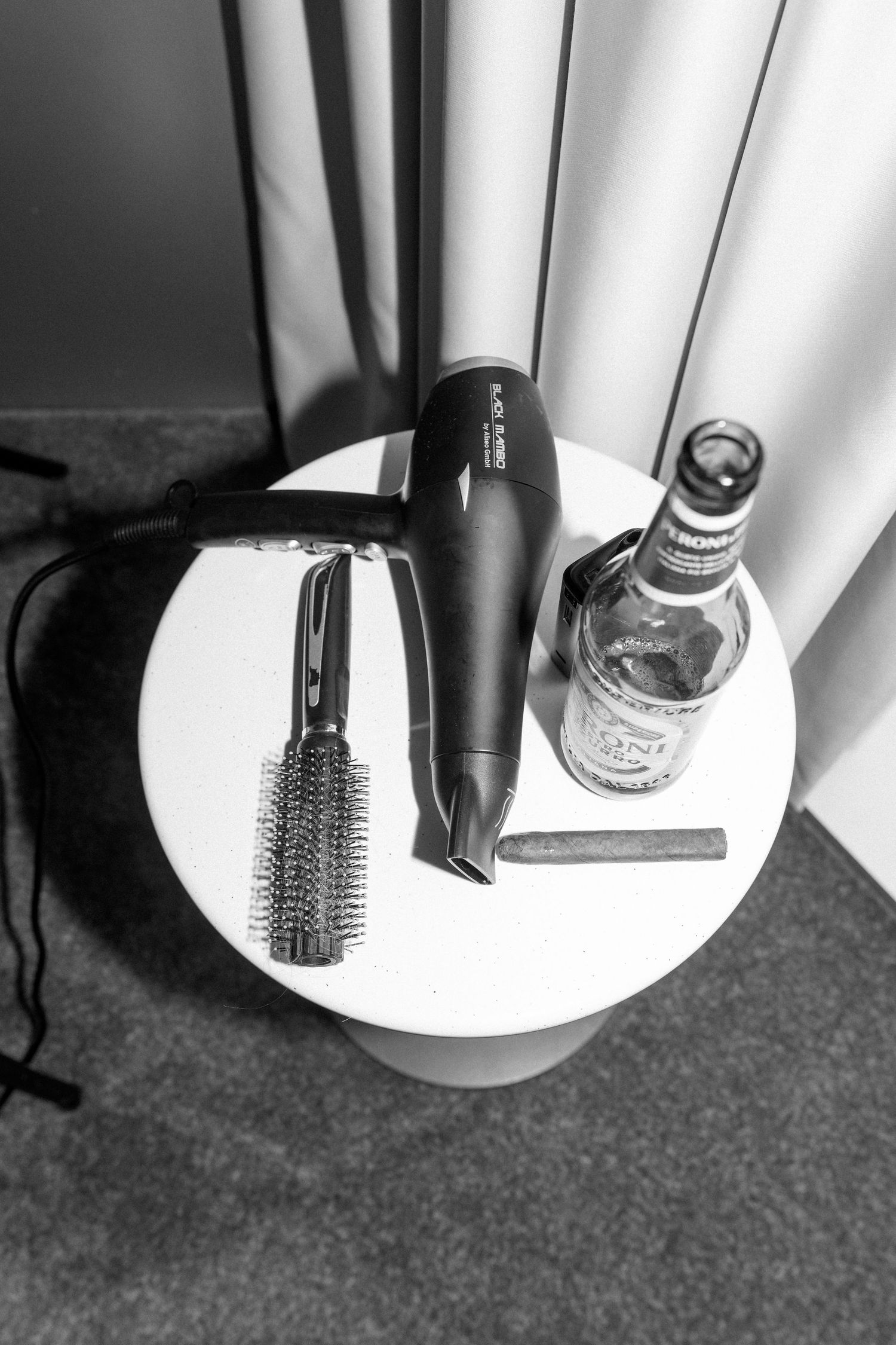 Black and white photo of hair styling tools and drink on white table.