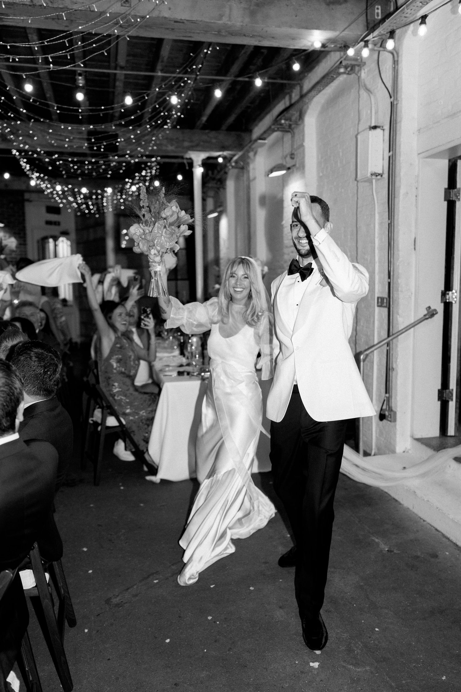 Wedding reception party with string lights overhead as guests dance and celebrate.