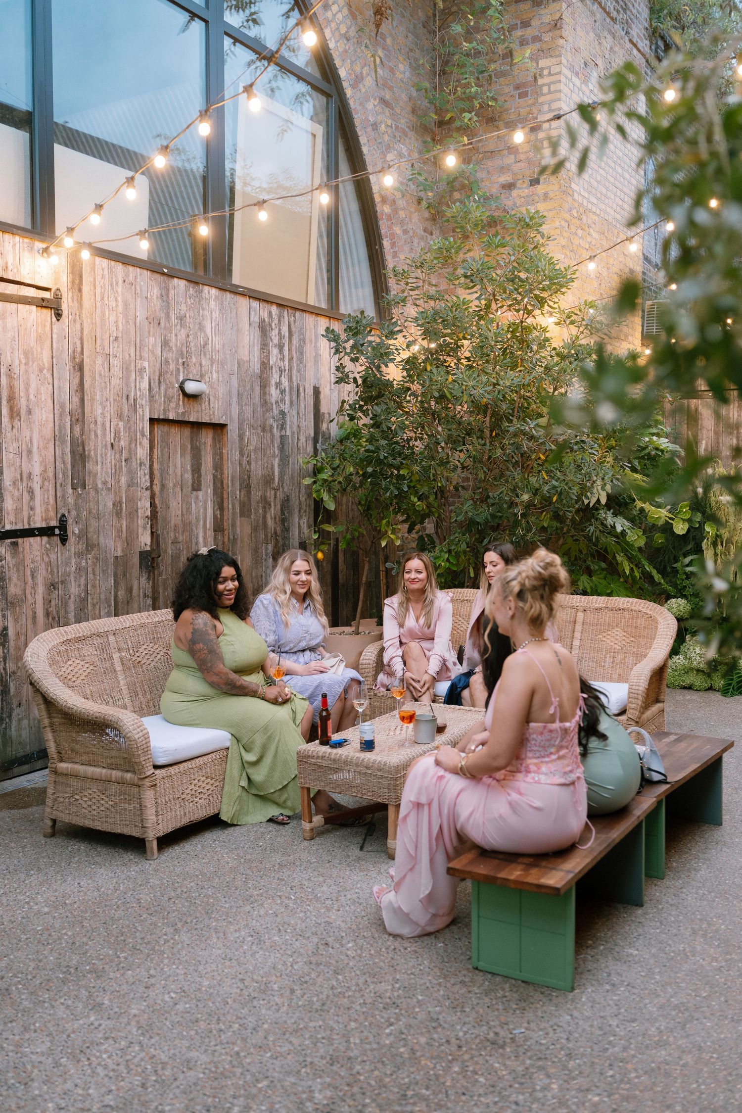 Outdoor lounge area with wooden benches and string lights where guests relax during an evening event.