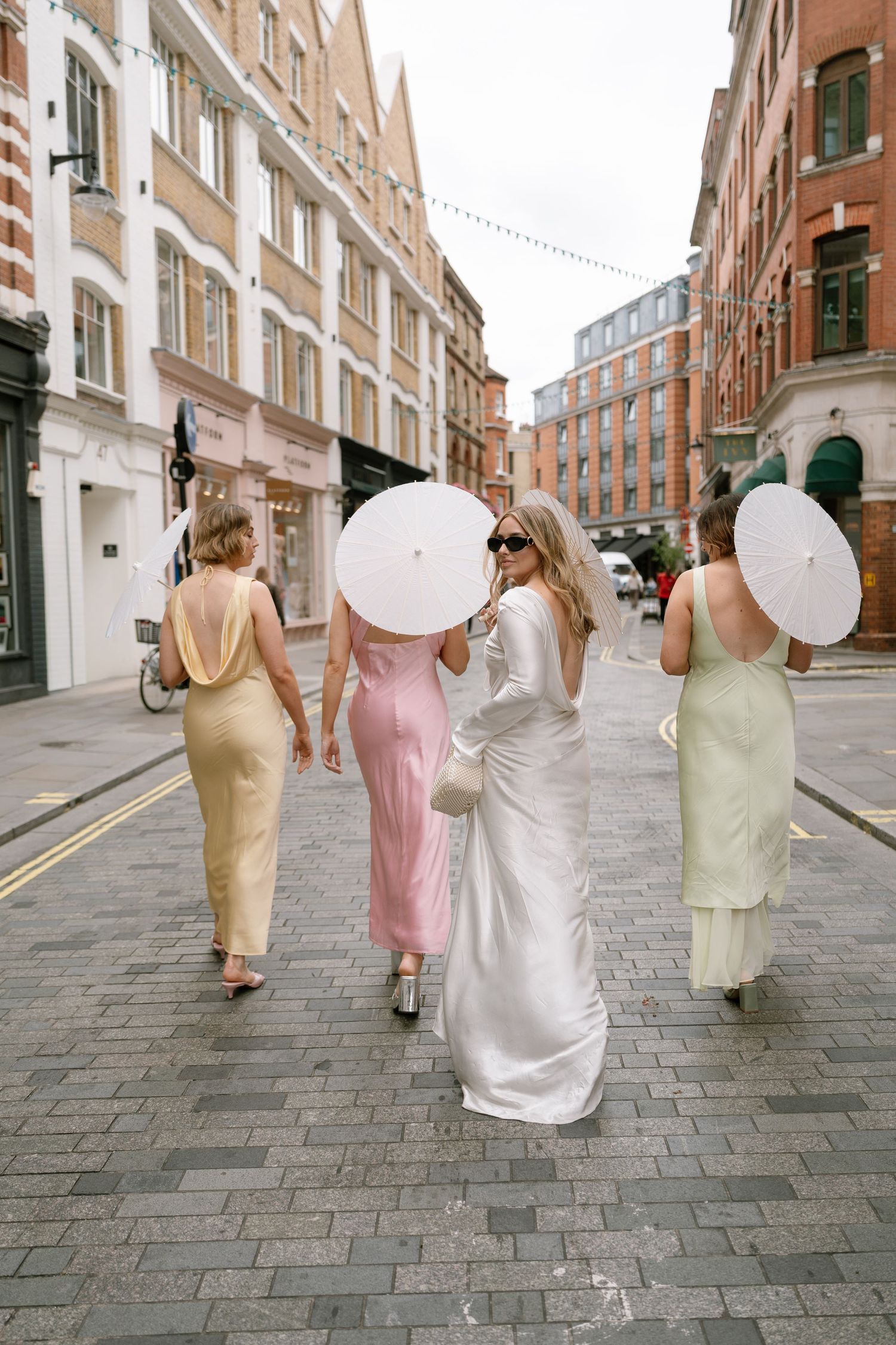 Wedding party walking down a cobblestone street in pastel dresses and formal attire.