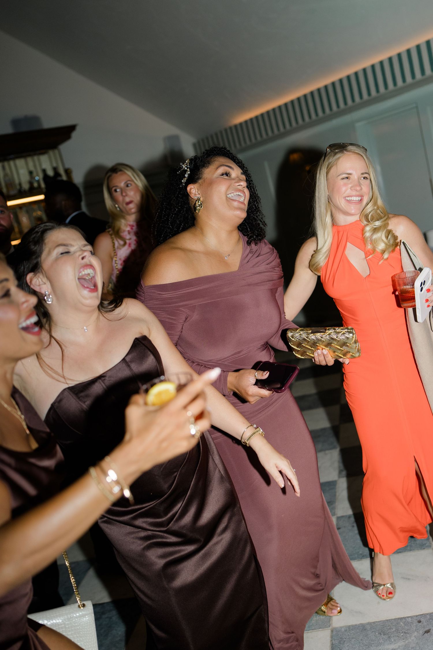 Wedding guests in satin gowns laugh and dance joyfully during evening wedding reception celebration.