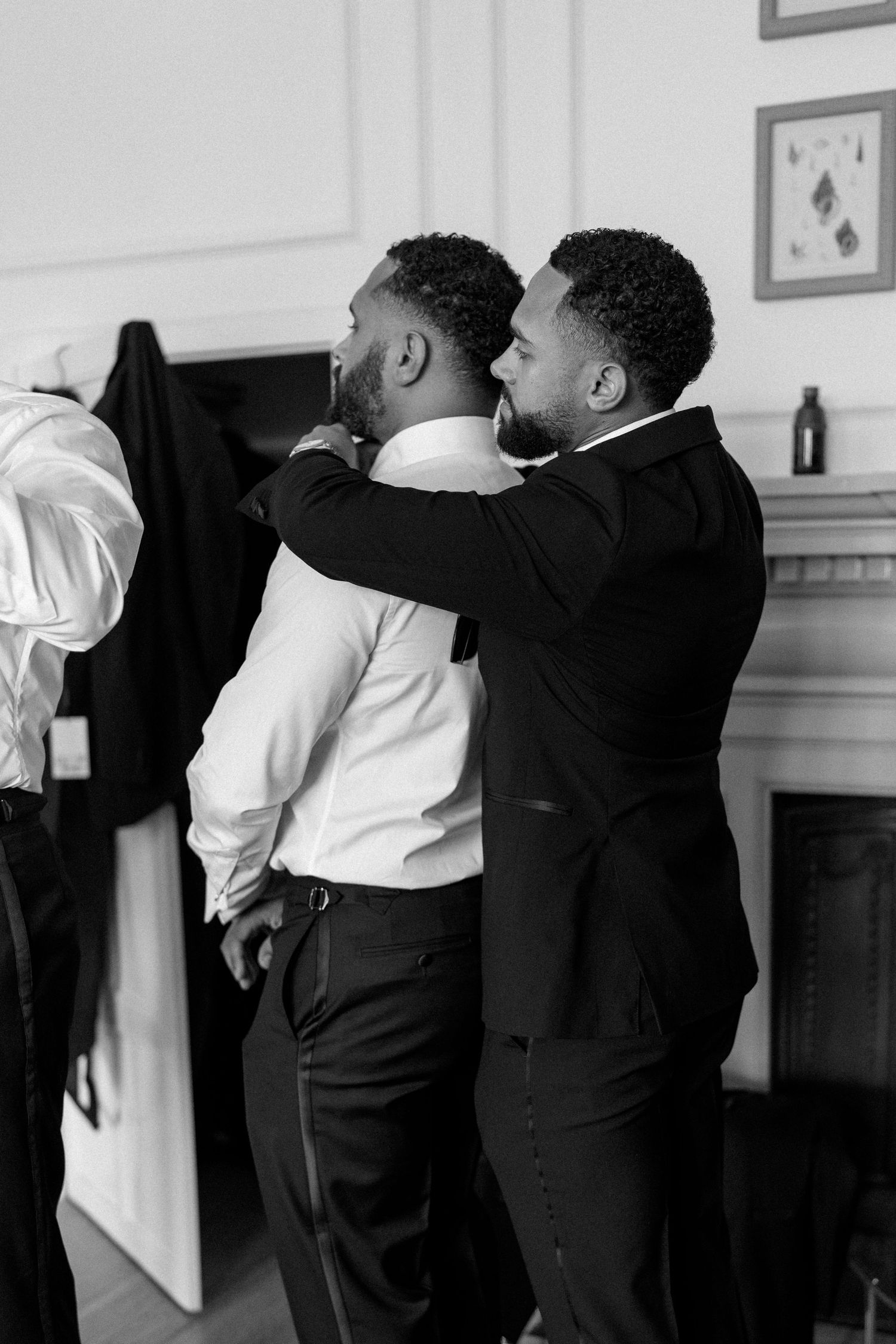 Black and white photo of groom helping groomsman with collar before wedding.
