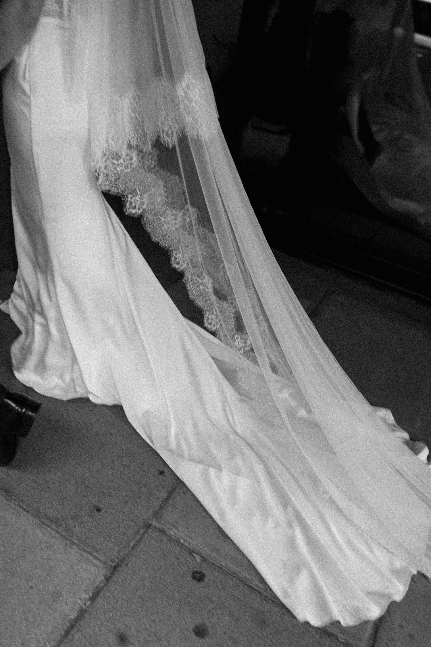 Close-up black and white detail shot of a brides elegant lace-trimmed wedding dress train and veil.