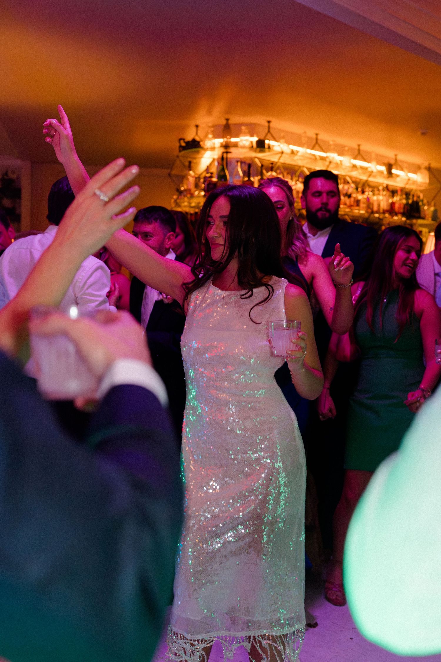 Bride in sequined fringe dress dances joyfully at a colorfully lit wedding reception.
