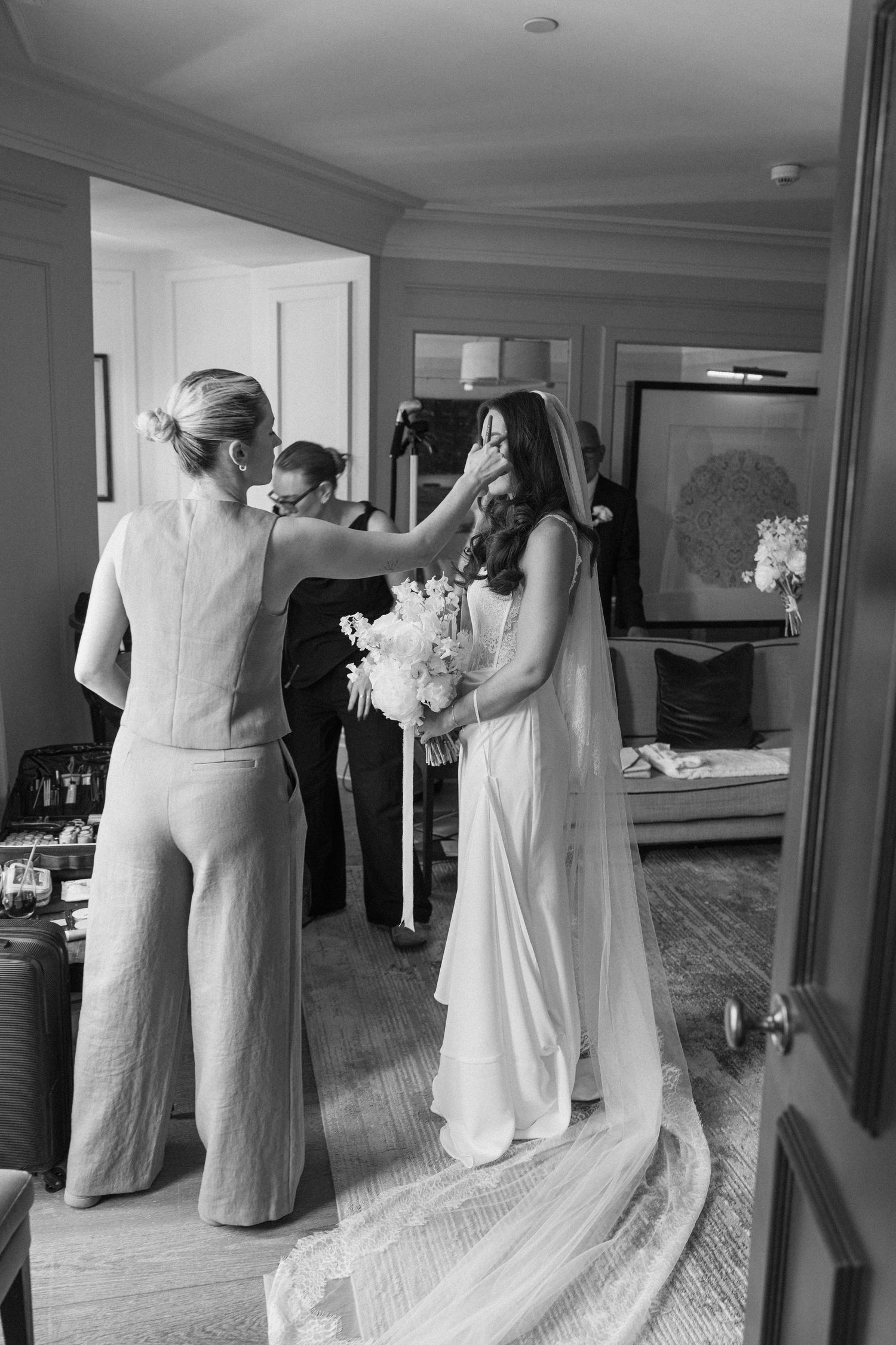 Black and white photo of a bridesmaid tenderly touching the brides face as she holds her bouquet before the ceremony.