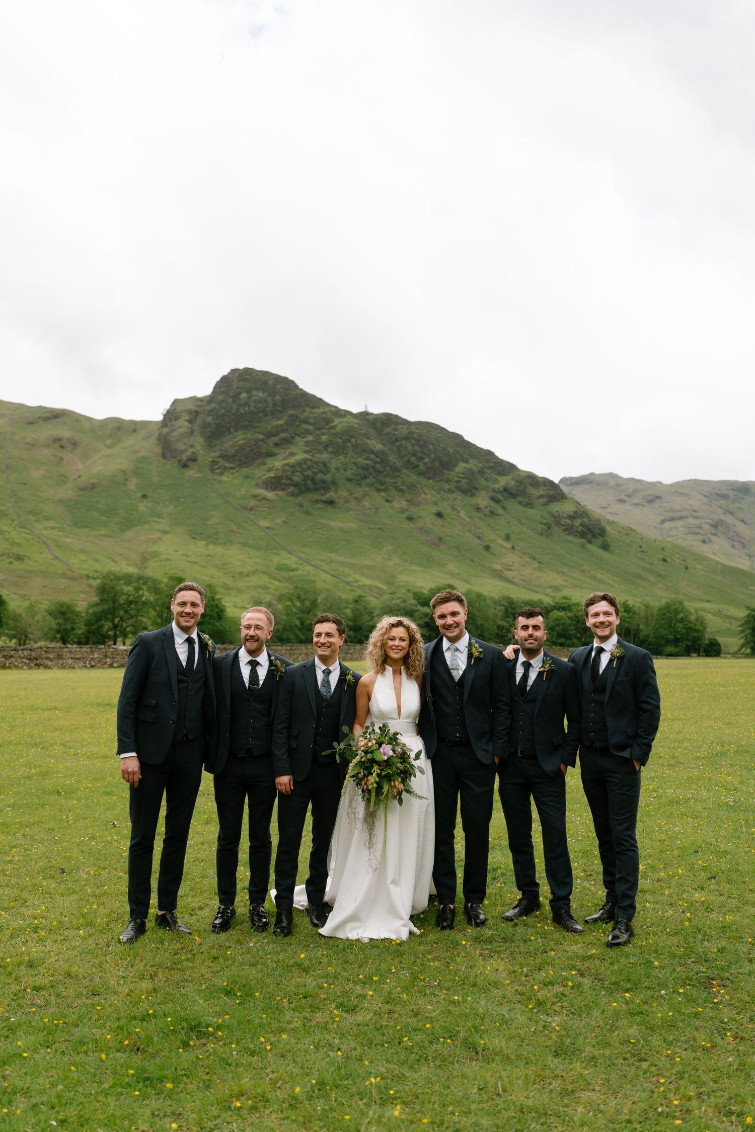 Wedding party portrait with groomsmen in black suits against a dramatic mountain backdrop.