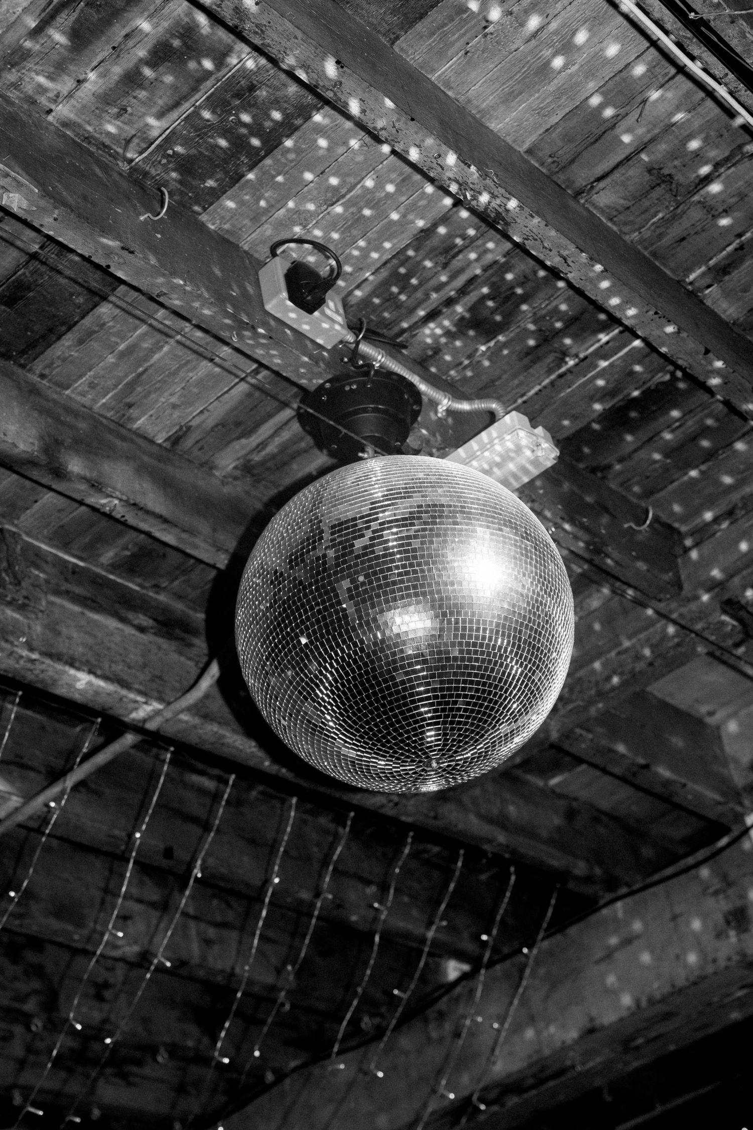 Sequence of disco ball hanging from wooden ceiling with string lights creating a party atmosphere.