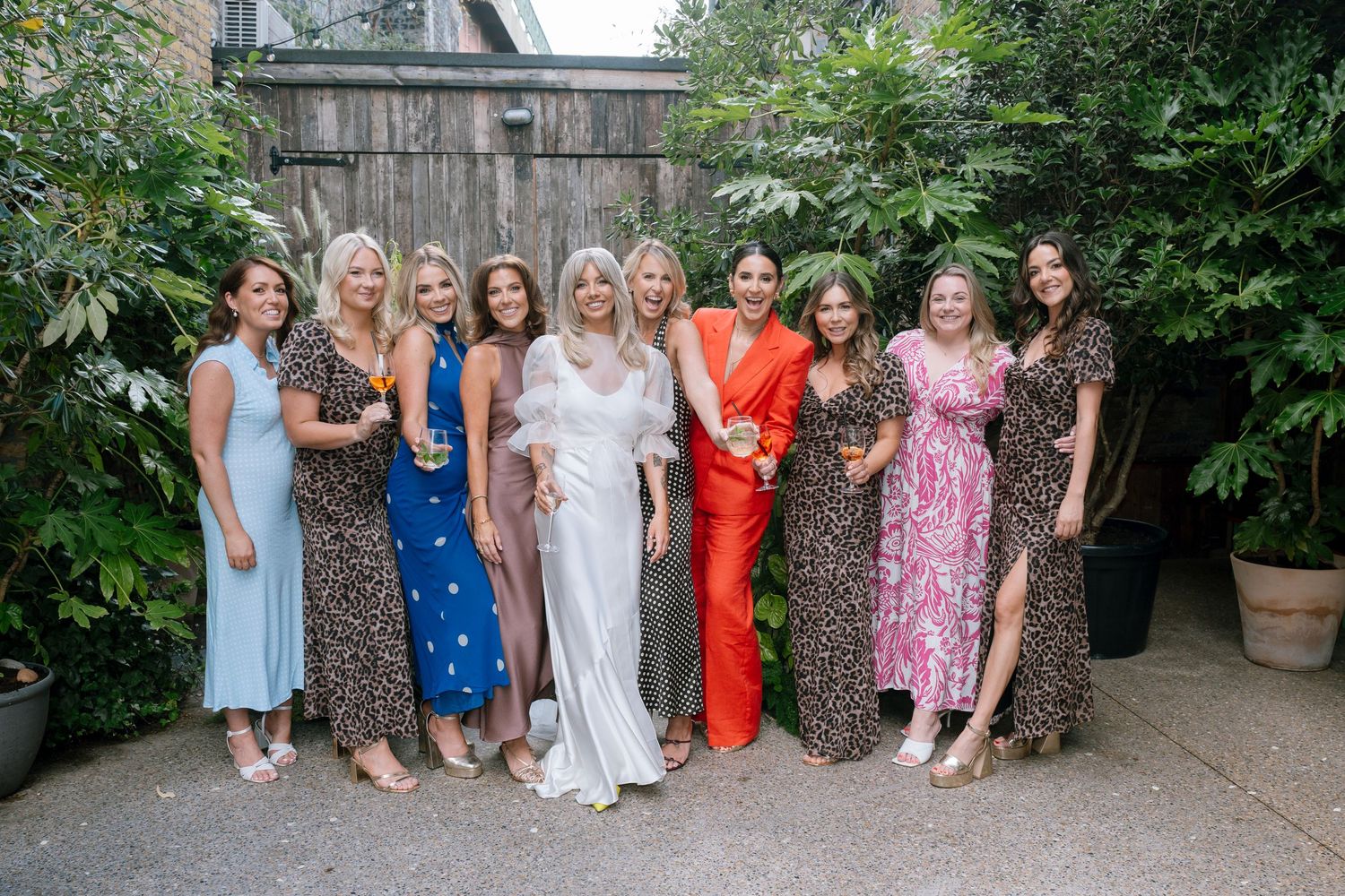 Wedding party members in colorful dresses pose together in a garden setting.