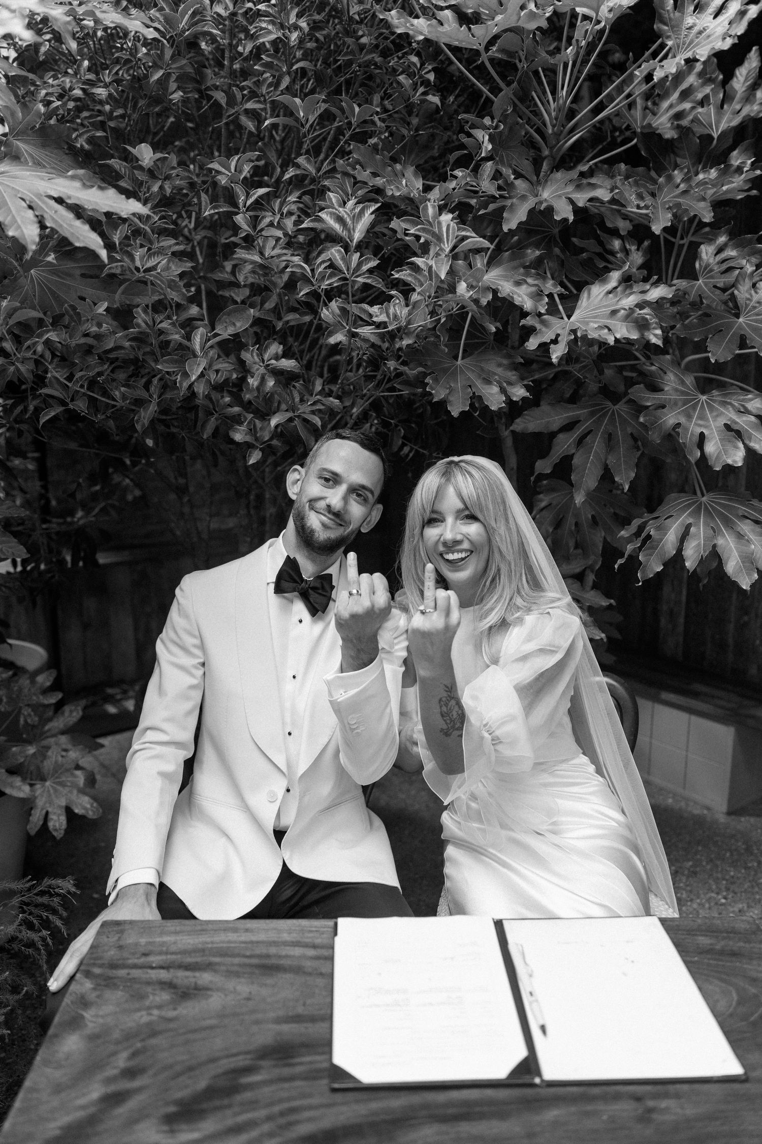 A couple in white formal attire signing documents during their wedding ceremony.