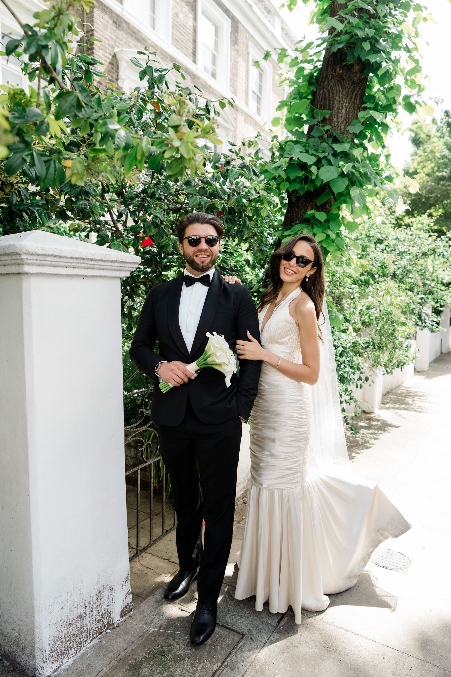 A couple poses for wedding photos in a garden setting with white columns.